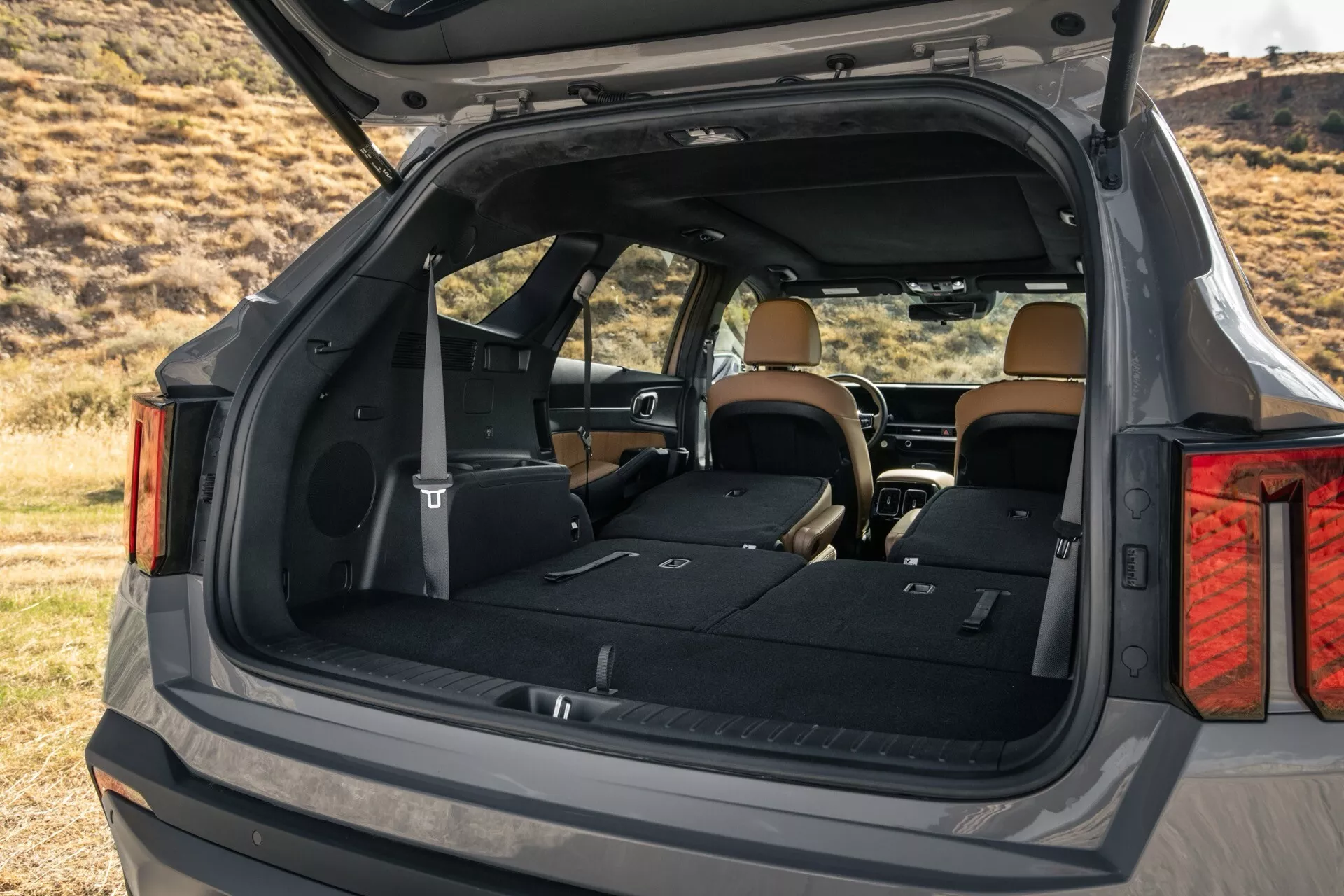 Kia Sorento MQ4 2024 po liftingu pokazująca przestronny bagażnik z ukośnego tylnego kąta, podkreślająca luksusowe i użytkowe cechy wnętrza z ciemną karoserią i jasnym wnętrzem