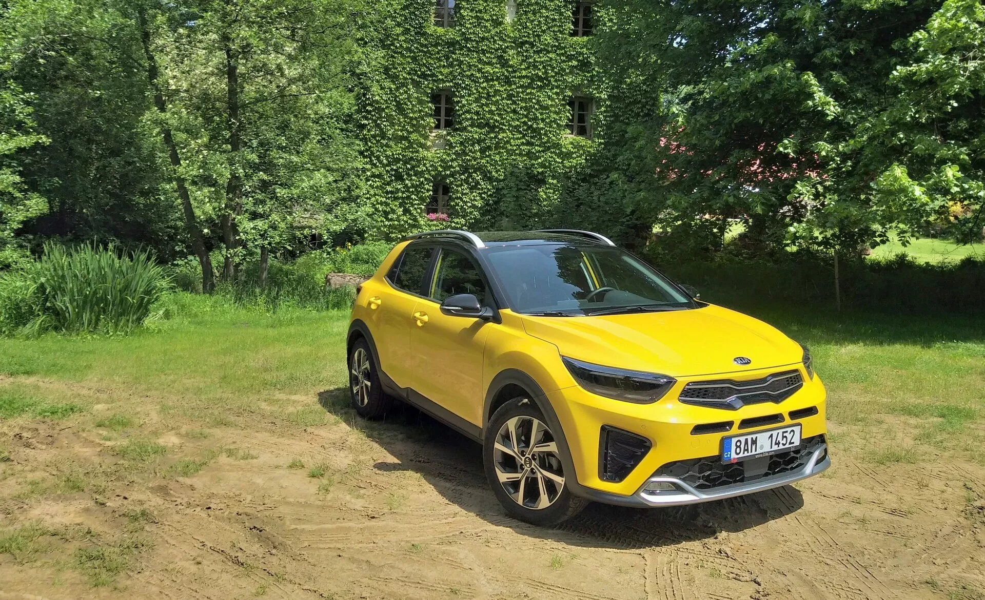 Jaskrawożółte SUV crossoverowe Kia Stonic 2017 w widoku z przodu pod kątem trzech czwartych, podkreślające jego przedni grill, reflektory LED, maskę oraz stronę kierowcy, umieszczone na tle naturalnym z światłem słonecznym na wolnym terenie, pokazujące zdolności do jazdy w terenie, sportowe koła z lekkich stopów i nowoczesne elementy projektowe.