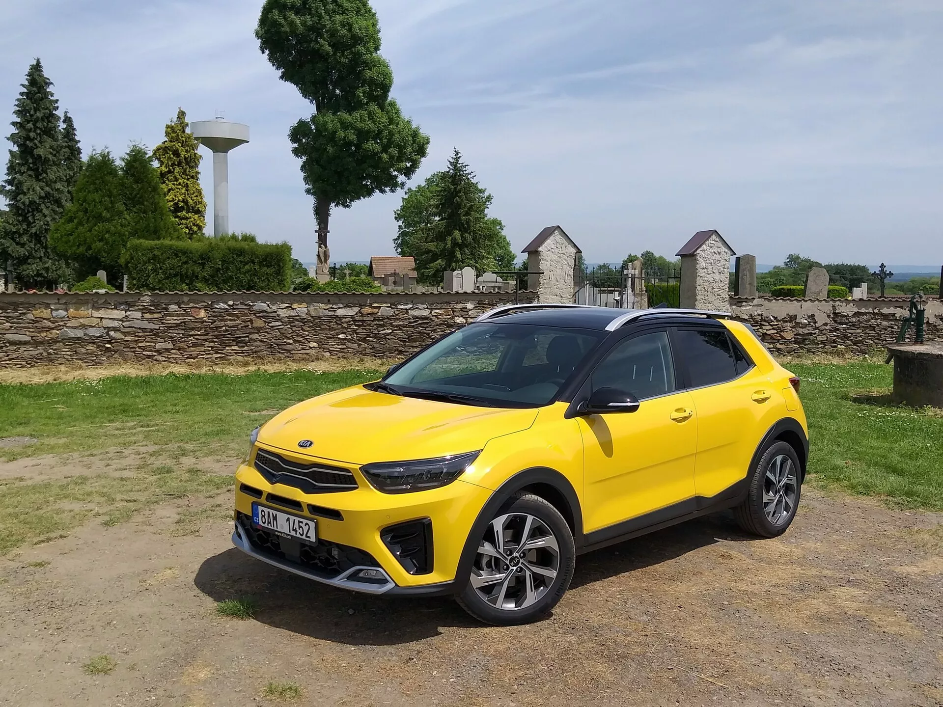 Kia Stonic 2017 w jasnożółtym kolorze, prezentująca swój przedni grill, reflektory LED, sportowy przedni zderzak oraz elegancki boczny profil z felgami ze stopu o wielu szprychach i relingami dachowymi, podkreślając estetykę kompaktowego crossovera i zaawansowane cechy projektowe pojazdu.