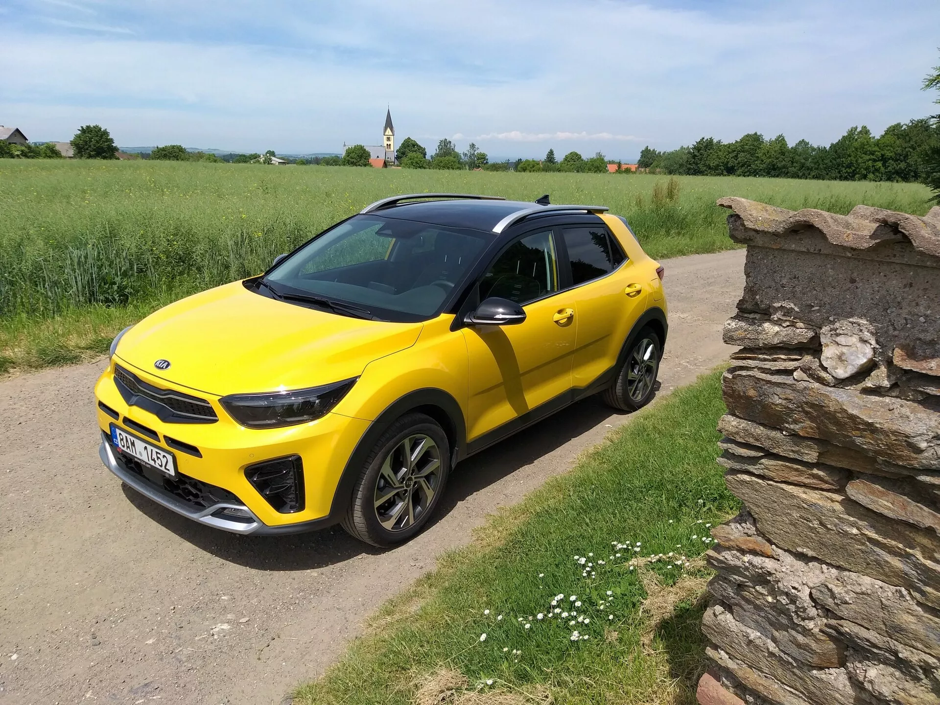Jasnożółty kompaktowy SUV Kia Stonic 2017 z czarnym dachem, prezentujący swój elegancki design i dynamiczne kontury z perspektywy trzech czwartych na wiejskiej drodze