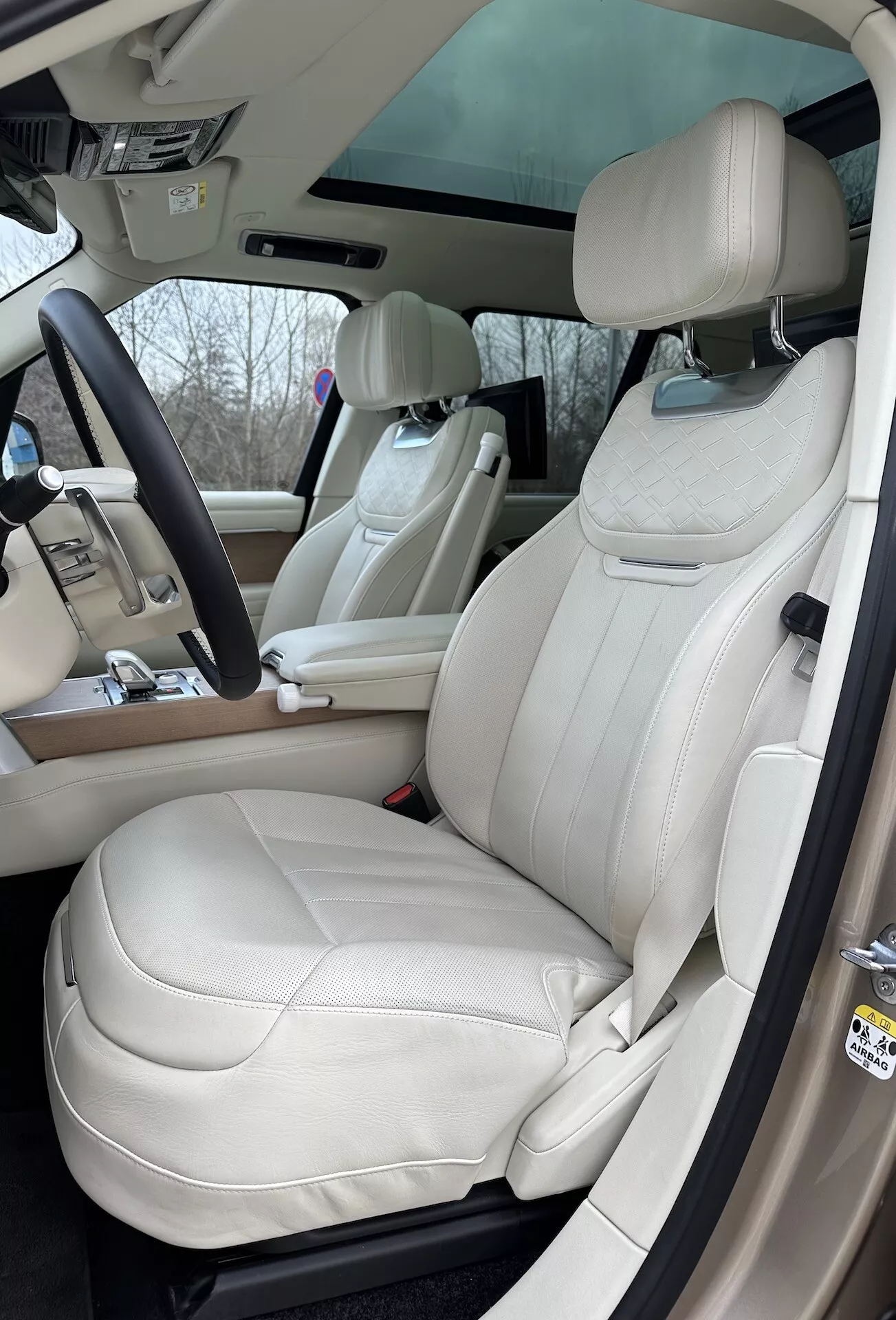 Widok wnętrza Land Rover Range Rover 2021 z akcentem na stronę kierowcy, luksusowe siedzenia z kremowej skóry, wielofunkcyjną kierownicę i zaawansowane elementy sterujące na konsoli środkowej