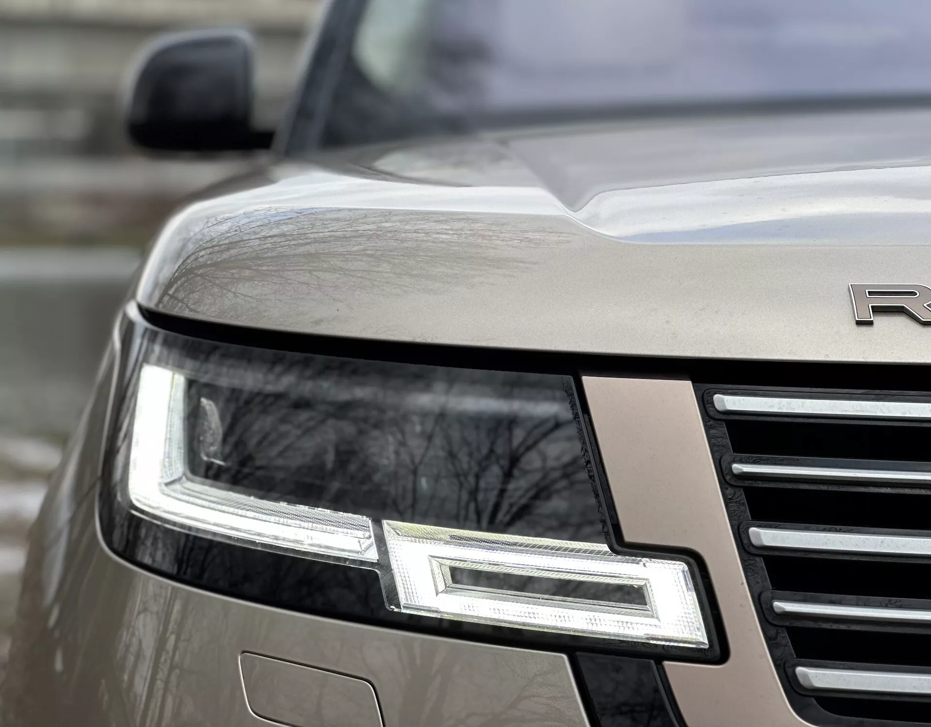 Zbliżony skośny widok na przedni róg Land Rover Range Rover 2021 z podświetlanym zespołem reflektorów LED, chromowaną kratą i częściowo widocznym emblematem na metalicznym nadwoziu
