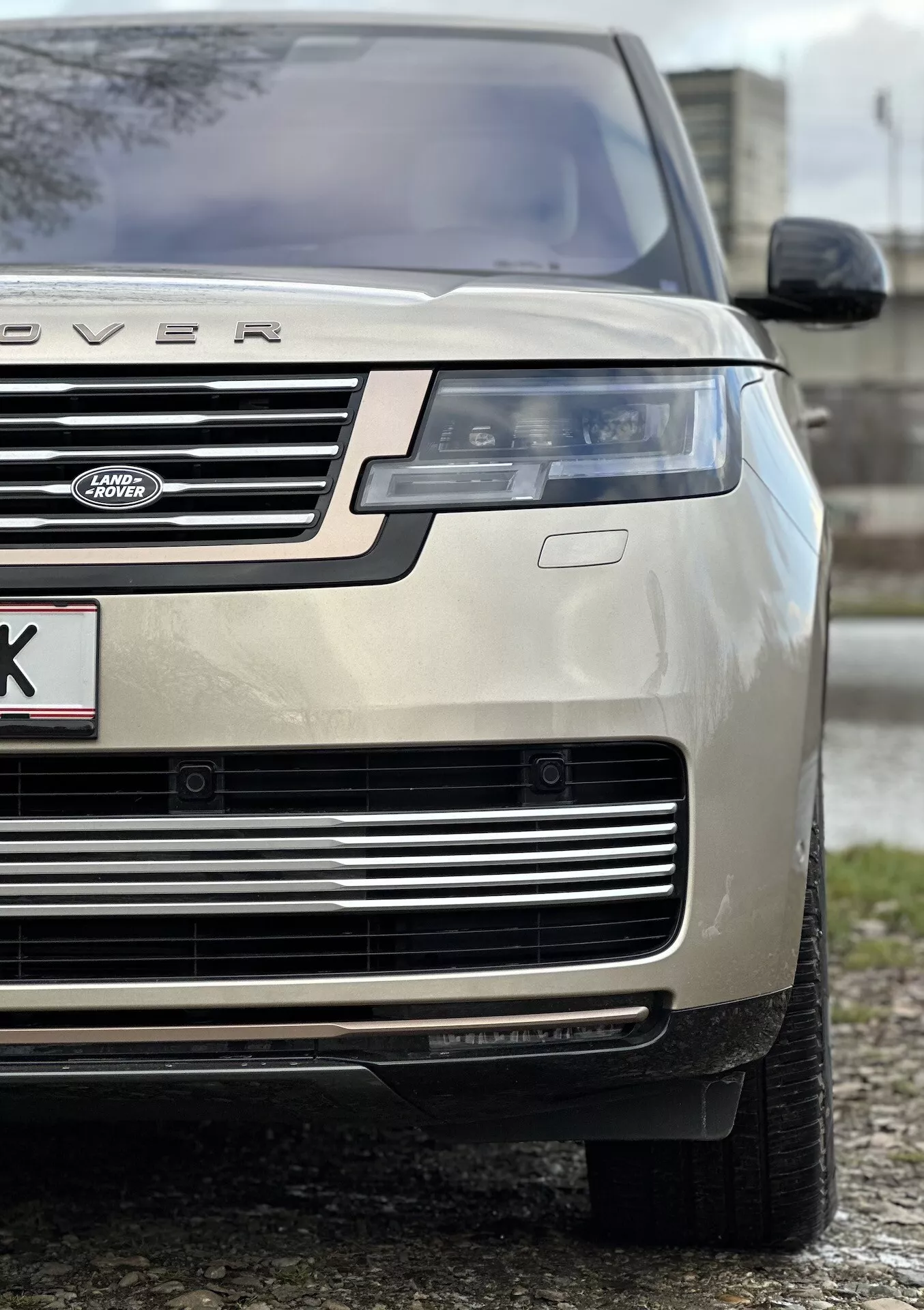 Zbliżenie na złoty Land Rover Range Rover 2021 na przedni lewy kwadrant, podkreślające wysokość i postawę pojazdu ze szczególnym uwzględnieniem maski, grilla, reflektora LED, zderzaka i opony całosezonowej, co wskazuje na luksus i zdolność do jazdy w terenie.