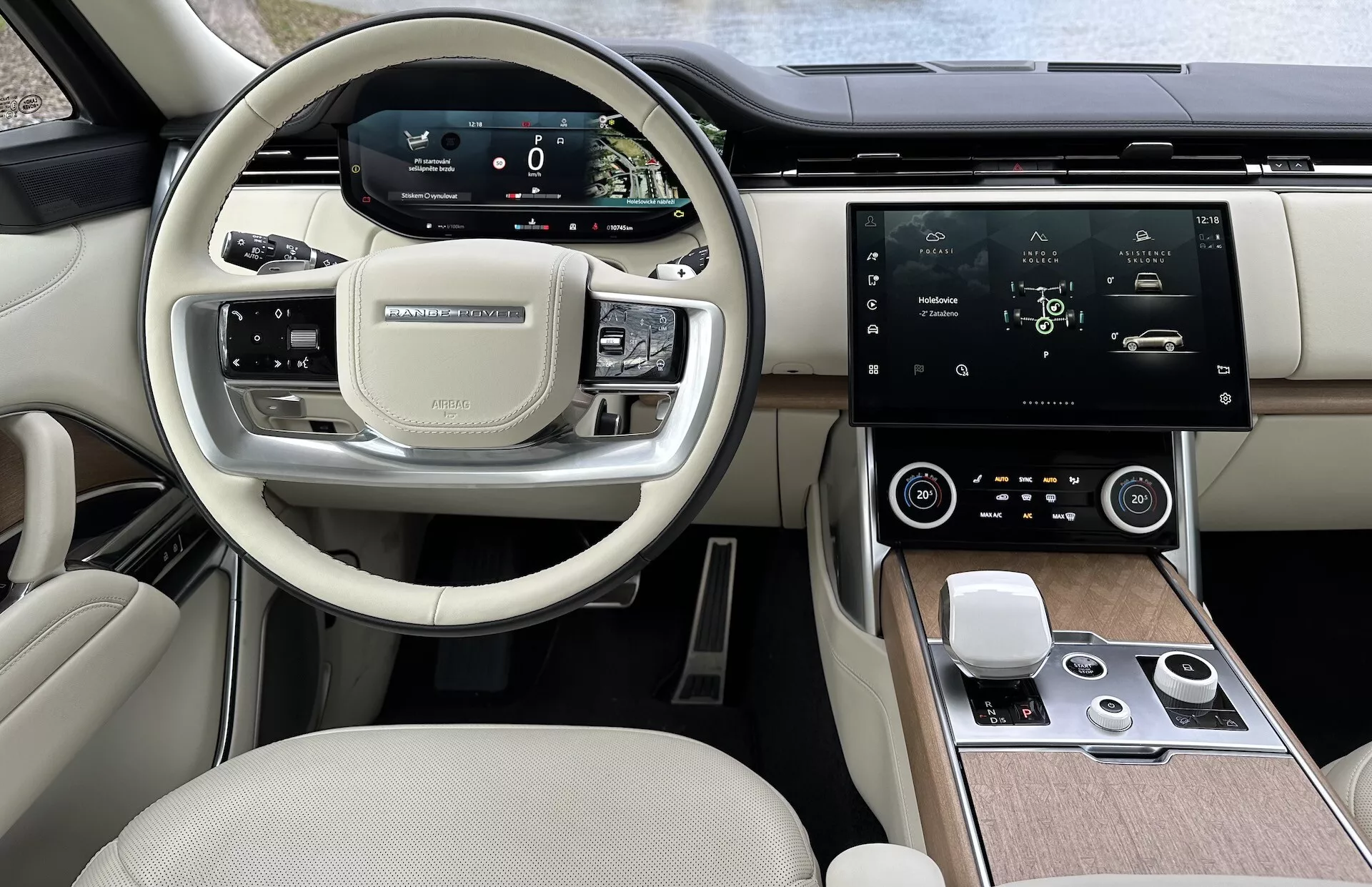 Wnętrze Land Rover Range Rover 2021 przedstawiające nowoczesną kierownicę z przyciskami wielofunkcyjnymi, cyfrowy zestaw wskaźników, duża centralna dotykowa konsola infotainment, automatyczna klimatyzacja i ekskluzywny dwukolorowy design kabiny