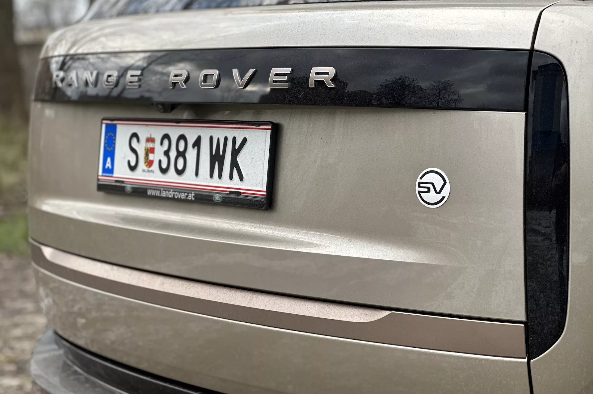 Zbliżenie na tylną klapę Range Rovera 2021 z napisem 'RANGE ROVER', europejską ramką tablicy rejestracyjnej, emblematem pojazdu elektrycznego oraz częścią tylnej lampy