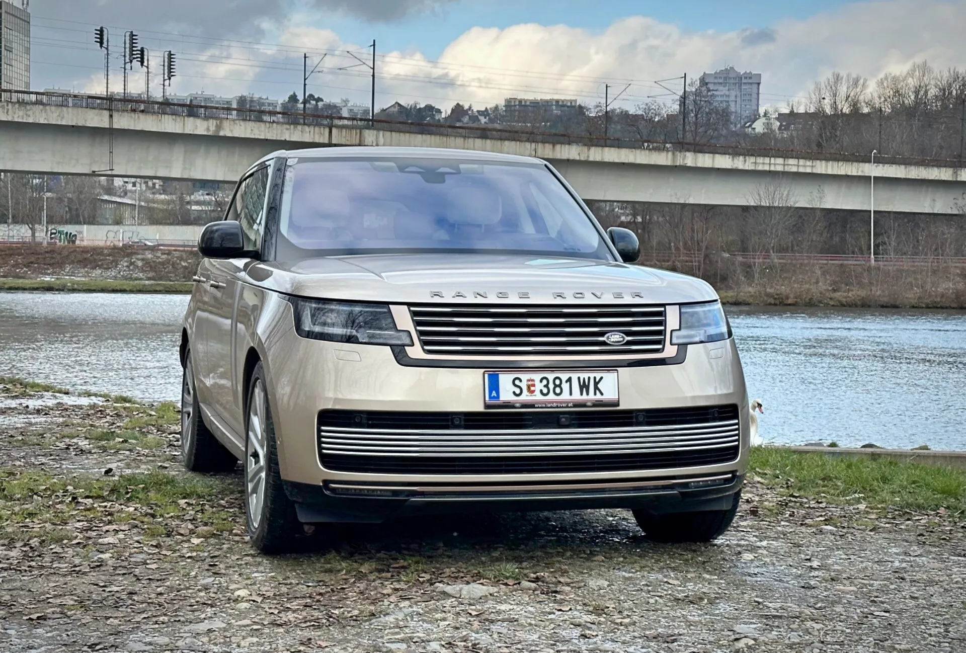Luksusowy SUV Range Rover 2021 zaparkowany na zewnątrz, w pobliżu rzeki i mostu, w miejskim otoczeniu, pokazujący jego nowoczesny design, przedni grill i eleganckie reflektory LED