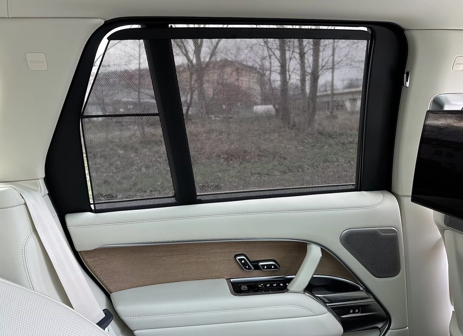 Wnętrze tylnej prawej strony Land Rover Range Rover 2021, z luksusowym designem w kolorach beżowym i czarnym, wykończeniami drewnianymi, końcówkami ze skóry, elektroniczną roletą przeciwsłoneczną i zaawansowanymi systemami kontroli