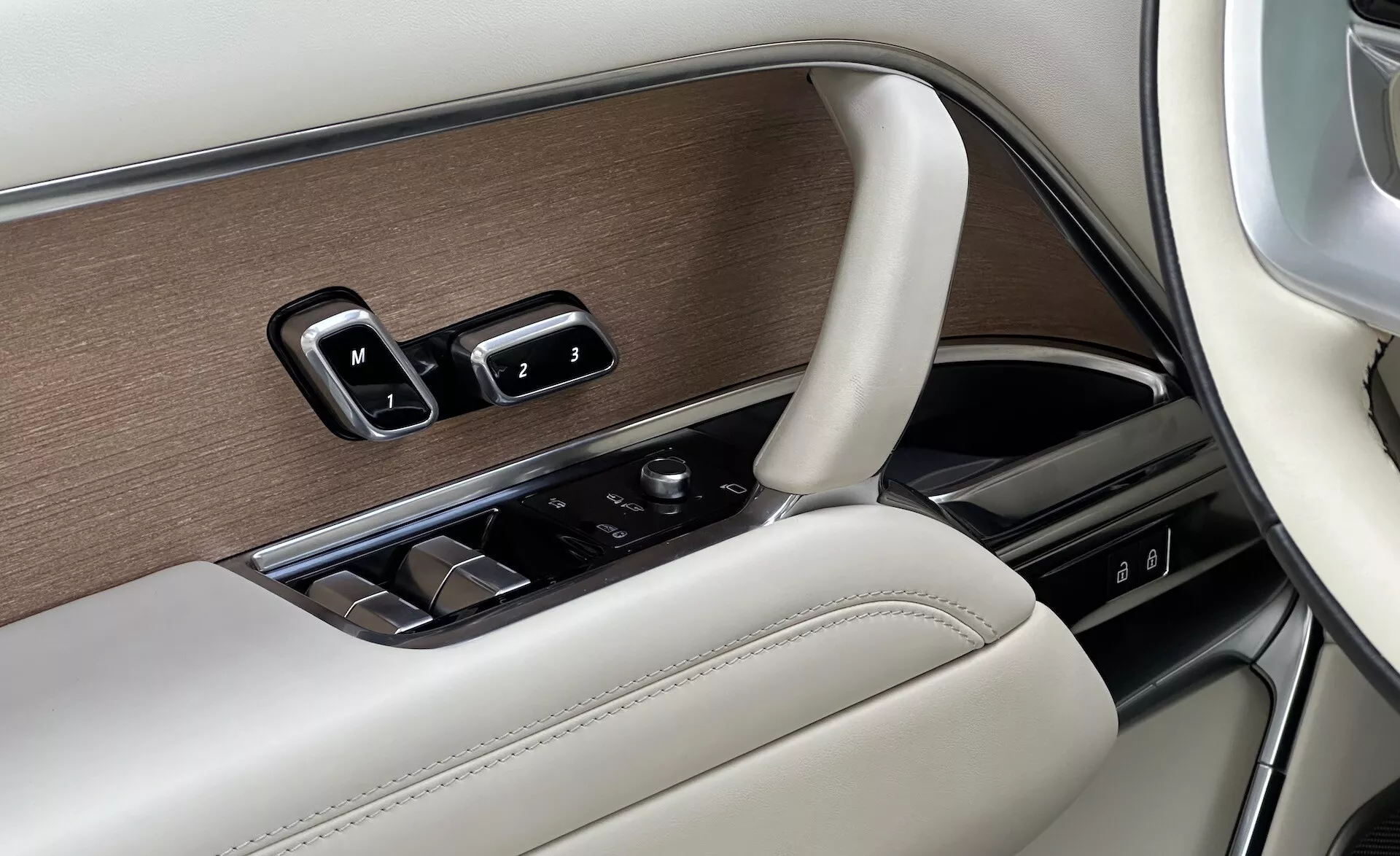 Szczegół wnętrza Land Rover Range Rover 2021 pokazujący panel drzwiowy strony kierowcy z kontrolami okien, regulacjami lusterek, ustawieniami pamięci siedzenia w luksusowym wykończeniu z drewna, chromu i skóry, oraz pokrętłem sterującym do systemu infotainment.