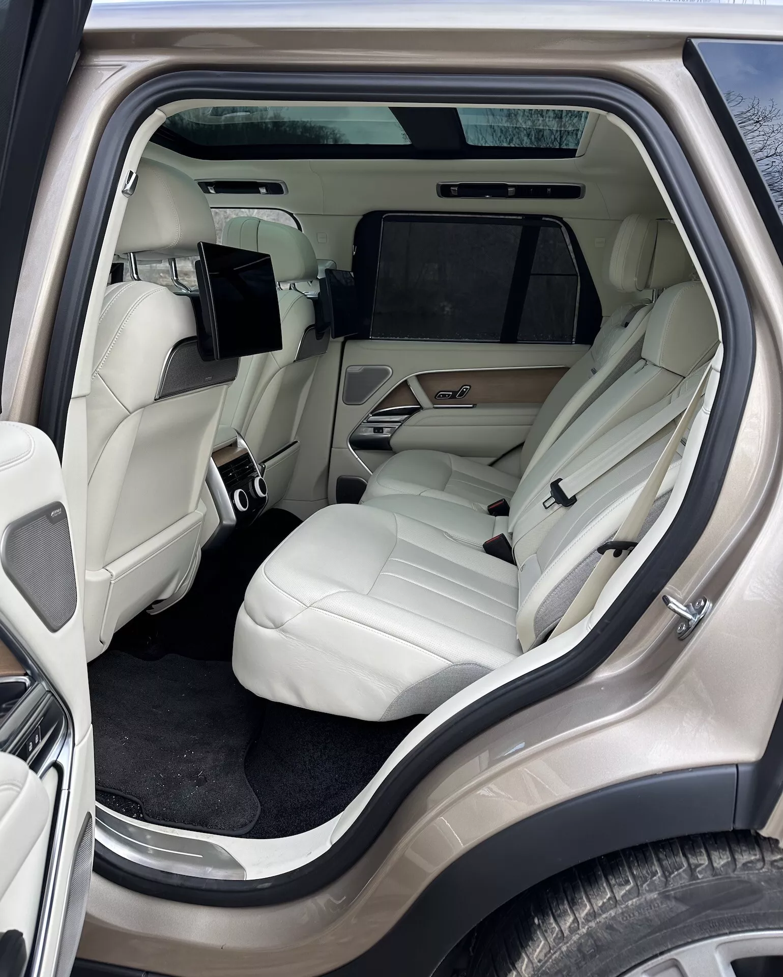 Widok wnętrza Land Rover Range Rover 2021 skupiający się na luksusowym przedziale pasażerskim z tyłu z zewnętrznego kąta bocznego, prezentujący jasne skórzane siedzenia, zaawansowaną konsolę środkową, system rozrywki i luksusowe detale