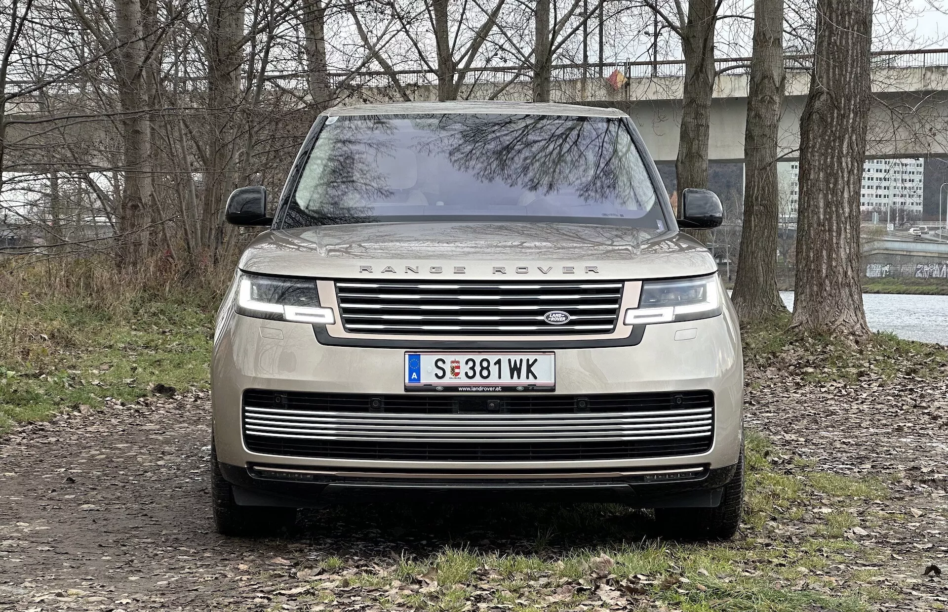 Widok z przodu Range Rovera 2021 pokazujący grill, reflektory LED, napis 'RANGE ROVER' na masce oraz zaparkowany na nieutwardzonej powierzchni z półwiejskim tłem