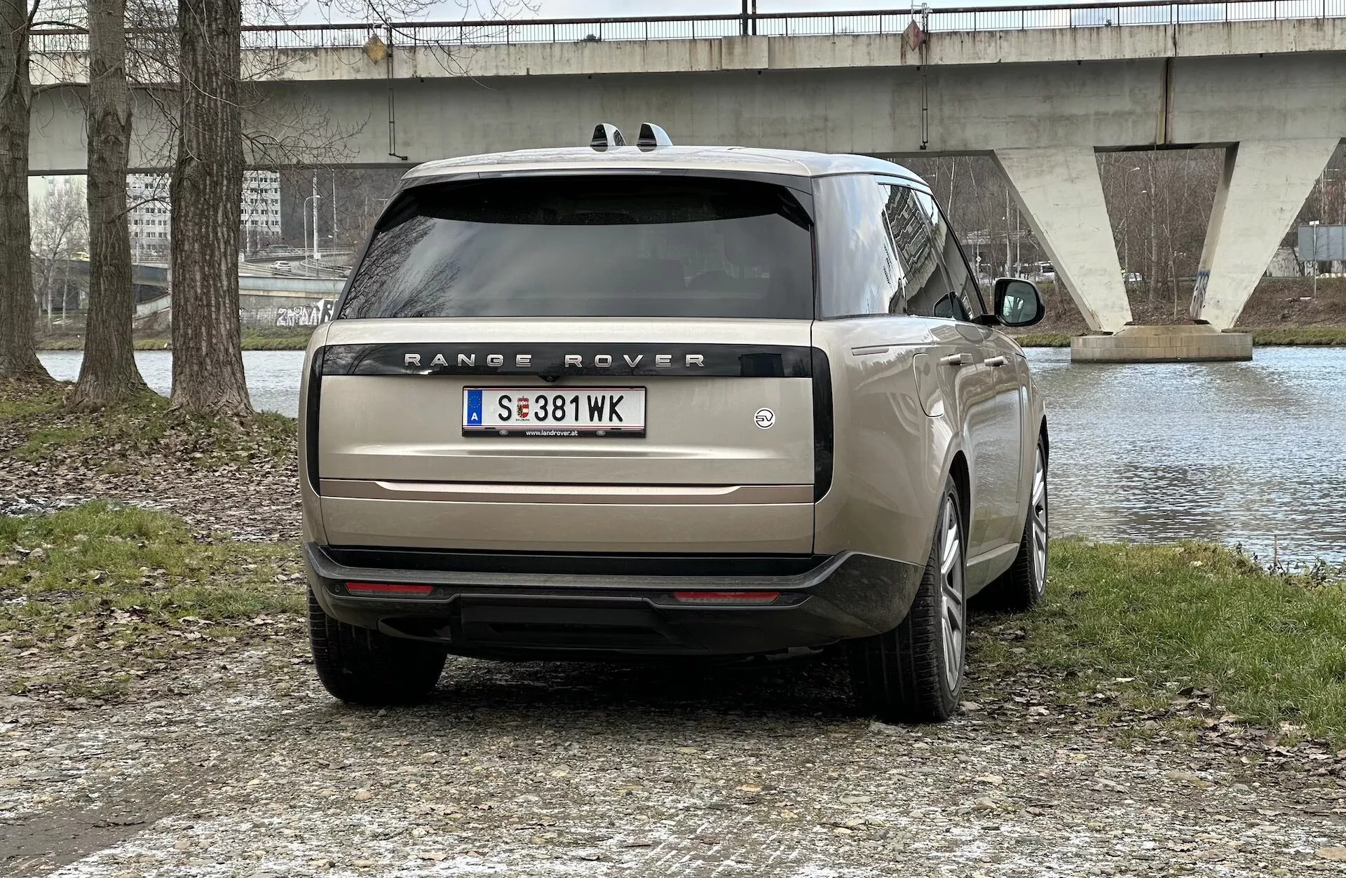 Tylny widok Range Rovera 2021 zaparkowanego na zewnątrz z widokiem na zbiornik wodny i most w tle, pokazujący diody LED świateł tylnych, podwójny wydech, przyciemniane szyby i wieloramienne felgi aluminiowe.