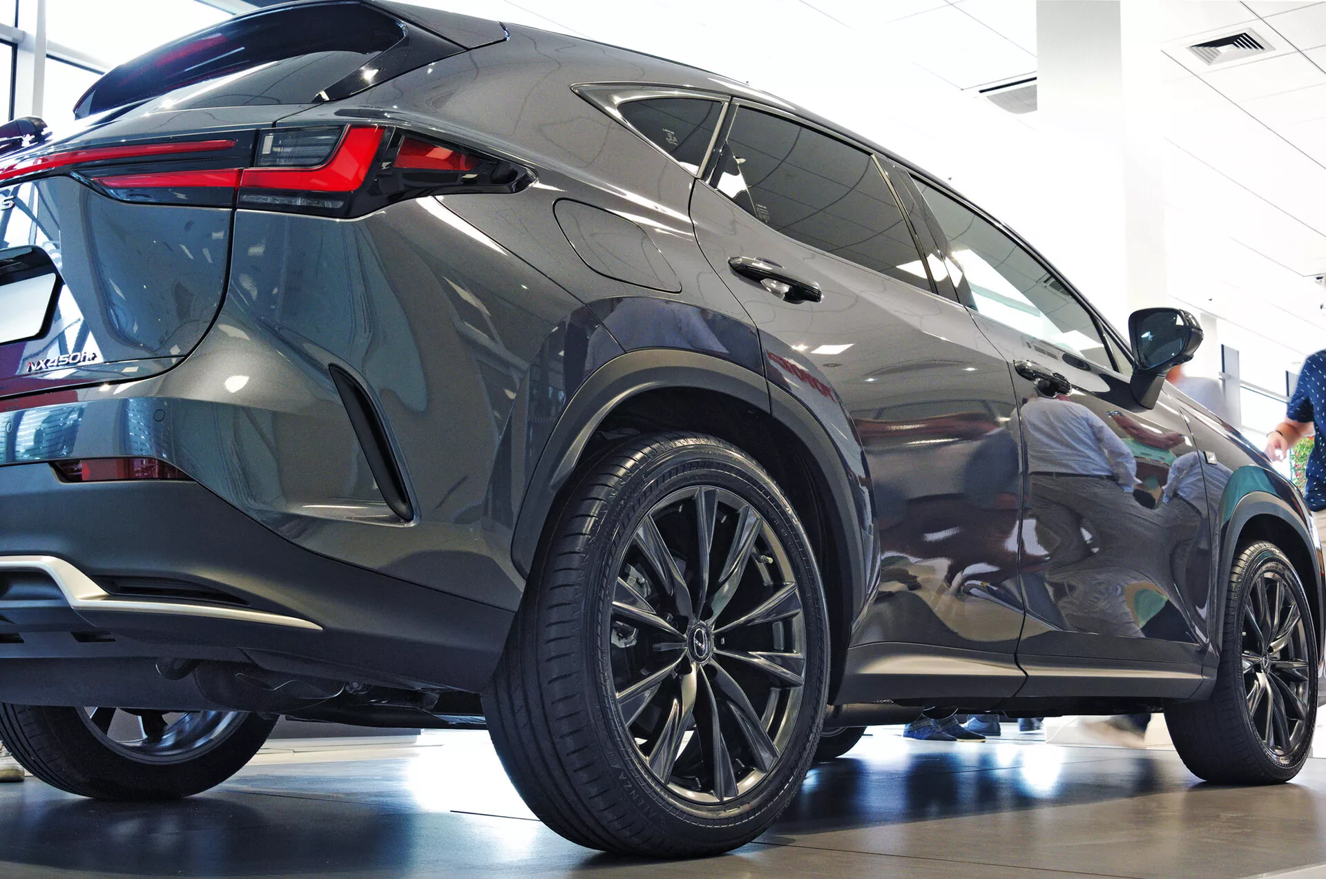 Tylny trójwymiarowy kąt Lexusa NX 2021 SUV pokazujący profil boczny i tylny z dużymi wieloramkowymi felgami aluminiowymi, niskoprofilowymi oponami, ostrymi kątami tylnymi światłami LED, metaliczną karoserią, przyciemnianymi szybami, zintegrowanym tylnym spoilerem i wypolerowanym środowiskiem salonu podkreślając nowoczesną estetykę i luksusowe cechy