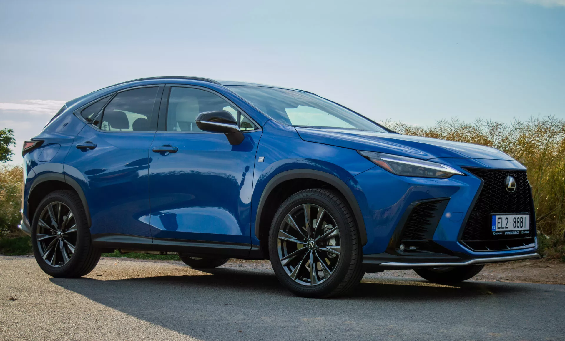 Kompaktowy SUV Lexus NX 2021 w żywym niebieskim kolorze, przedstawiający przedni zderzak, grill, światła LED, maskę, koła i linie konturu boczne z widoku z przodu pod kątem trzech czwartych na zewnątrz w świetle dziennym