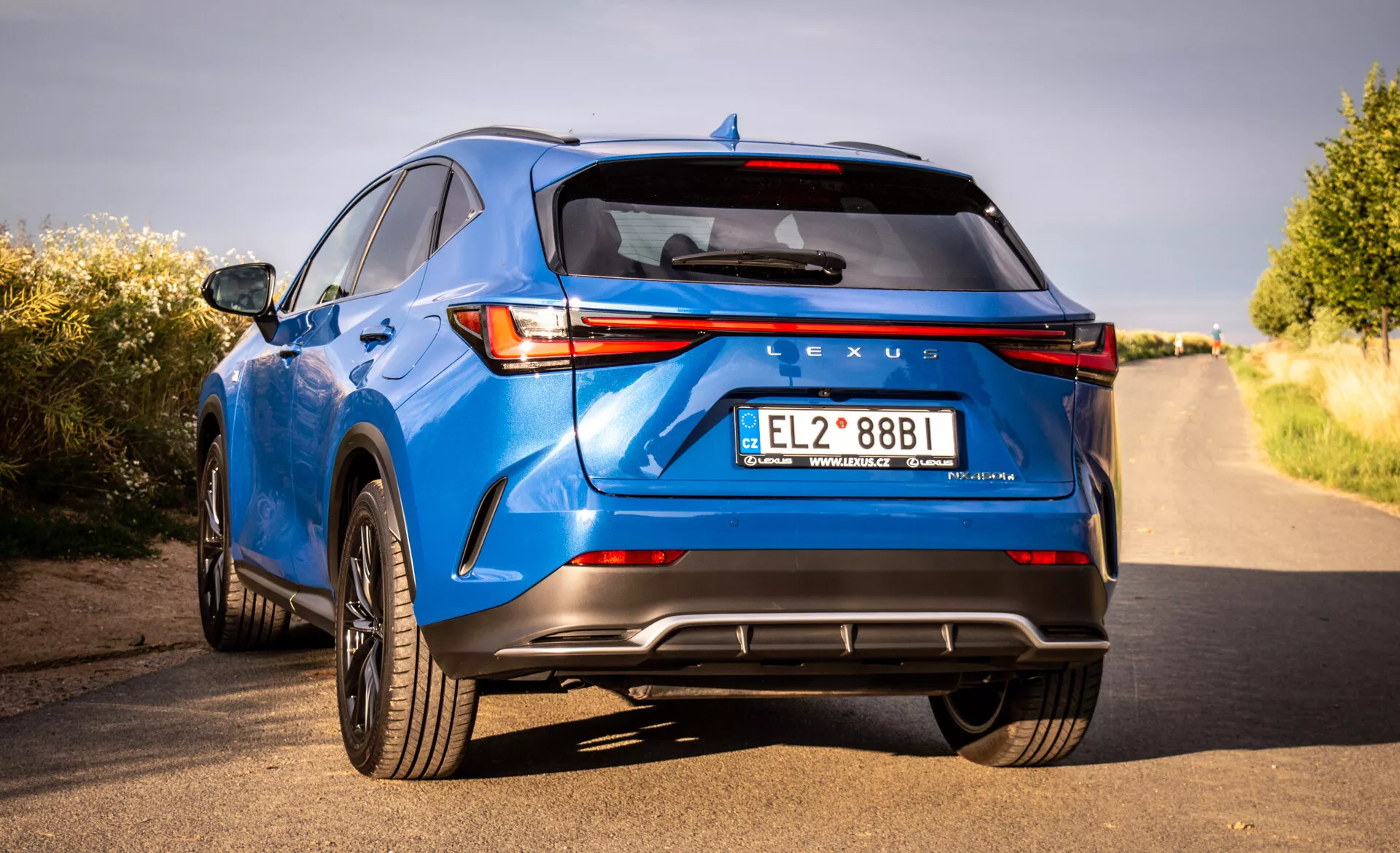Tylny widok luksusowego SUV-a Lexus NX w kolorze niebieskim z 2021 roku z LEDowymi światłami tylnymi, brandingiem Lexus, sportowym zderzakiem tylnym z dyfuzorem, podwójnymi rurami wydechowymi i innymi cechami technologicznymi i projektowymi z perspektywy trzech czwartych z niskiego punktu widzenia