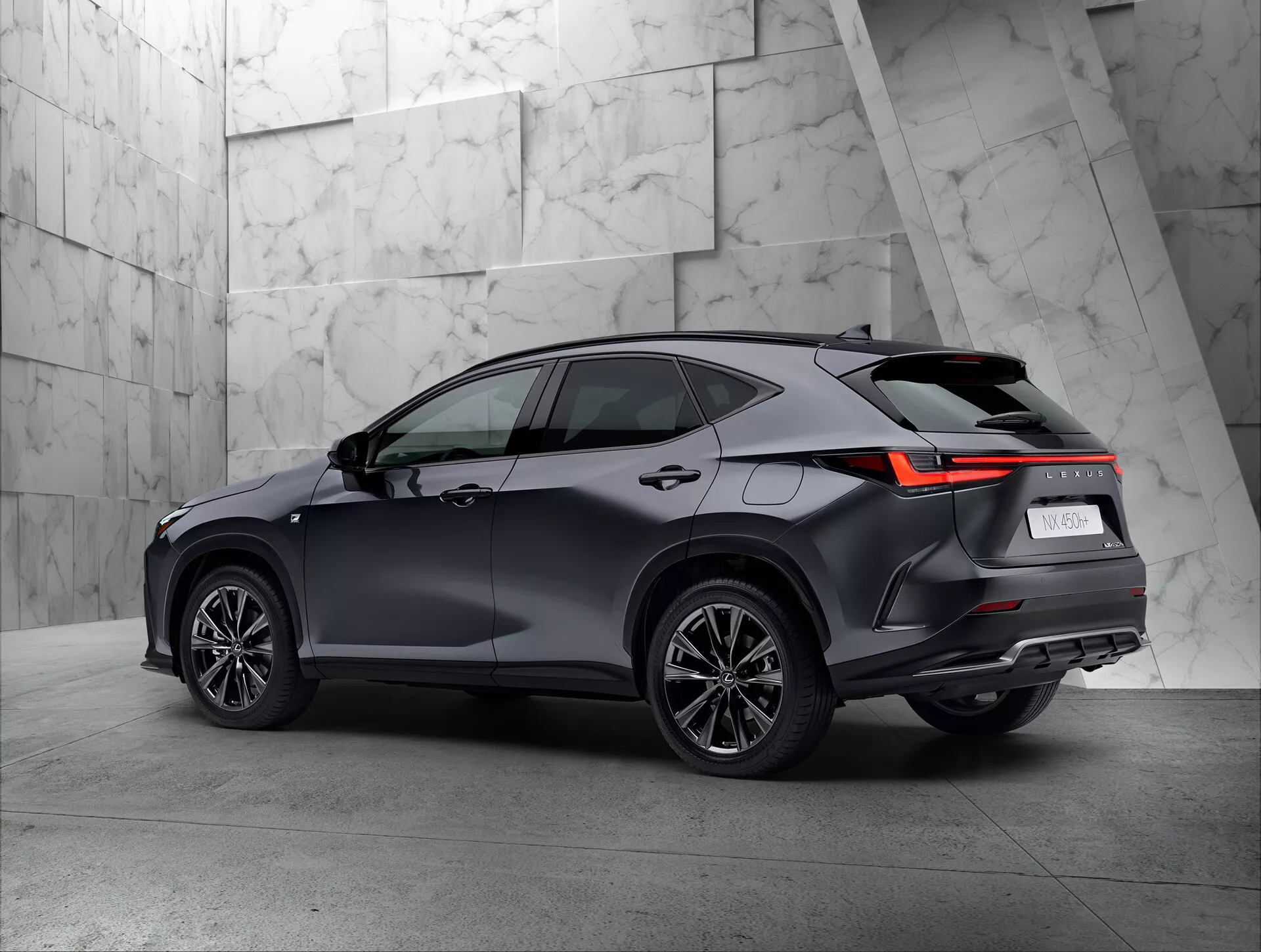 Trzy-czwarte widok tył nowoczesnego SUV-a Lexus NX 2021 w ustawieniu showroomu. Pojazd wyraźnie pokazuje prawą stronę i tył, prezentując tylne światła z kątowym projektem LED, ciemny, błyszczący lakier, wieloramienne koła i linię dachu z możliwymi relingami dachowymi. Neutralne, teksturowane tło dobrze kontrastuje z wyrafinowanym designem SUV-a.