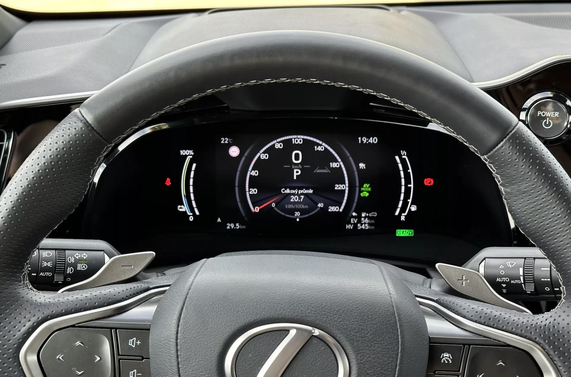Widok z miejsca kierowcy na kierownicę i cyfrowy panel instrumentów Lexusa NX 2021, podkreślający wskaźniki technologii hybrydowej, przyciski kontroli komfortu i ergonomiczny design wnętrza