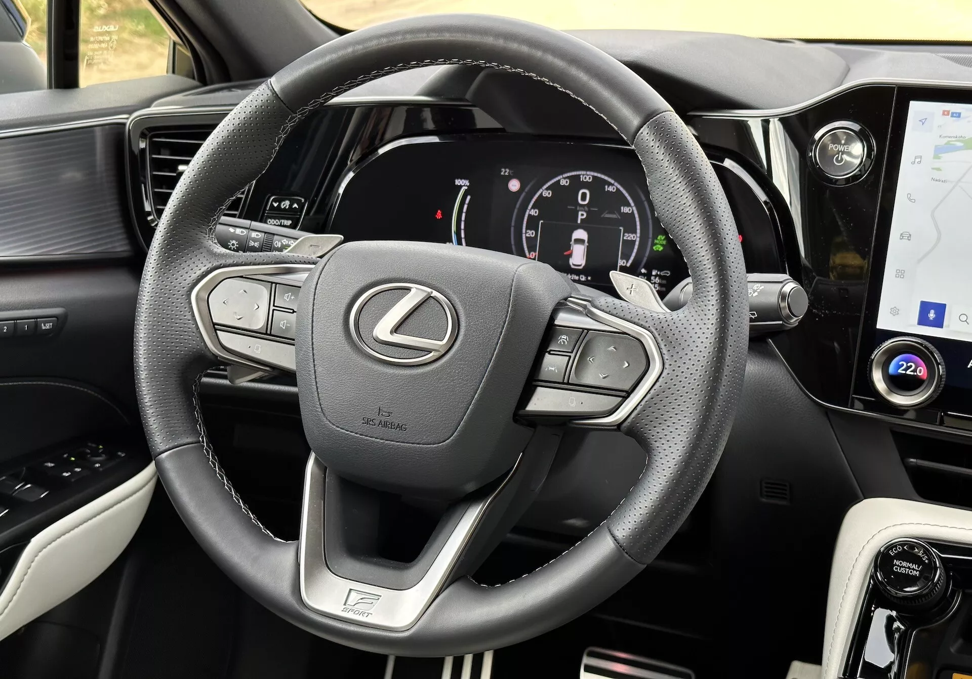 Widok wnętrza Lexusa NX 2021 ze skupieniem na kierownicy i desce rozdzielczej, prezentujący przyciski wielofunkcyjne, cyfrowy zegar, ekran dotykowy systemu infotainment, akcenty skórzane, selektor trybów jazdy, wyloty powietrza i szczegółowe szwy.