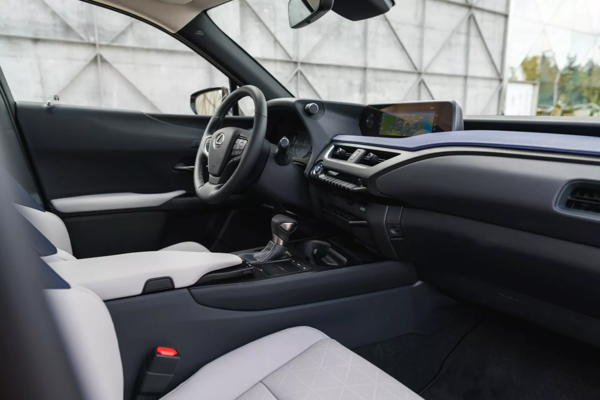 Nowoczesne wnętrze Lexusa UX 2019 z dwukolorowym wzornictwem, wielofunkcyjną kierownicą, wyeksponowanym ekranem infotainment i automatyczną skrzynią biegów z perspektywy nieco z boku, na wysokości wzroku