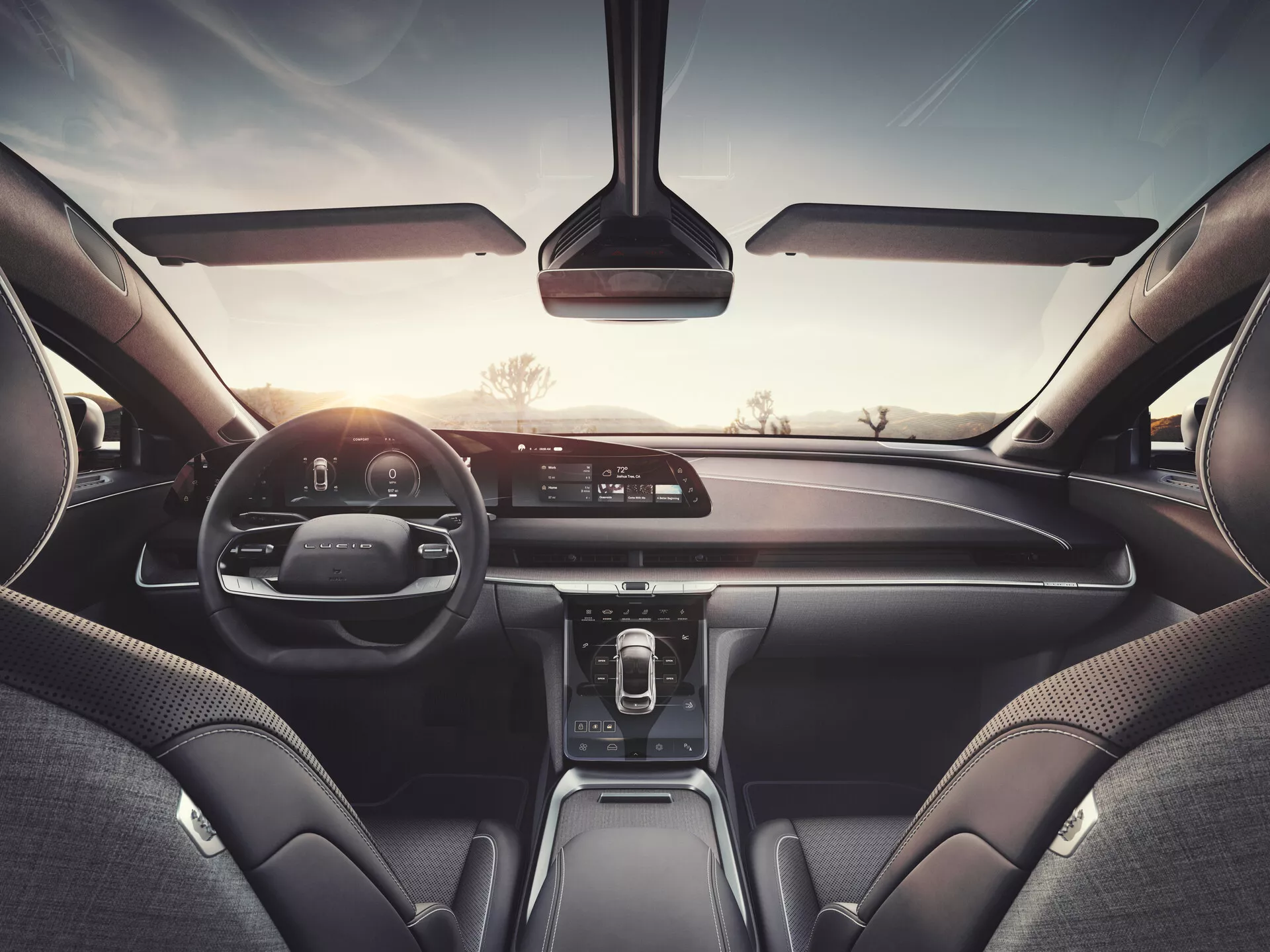 Widok wnętrza samochodu Lucid Air 2022 z tylnego siedzenia, ukazujący deskę rozdzielczą, wyświetlacz infotainment, cyfrowy zestaw wskaźników oraz skórzane i wysokiej jakości materiały, co sugeruje model wyższej klasy z zaawansowanym systemem multimedialnym, sterowaniem klimatyzacją i technologiami łączności.