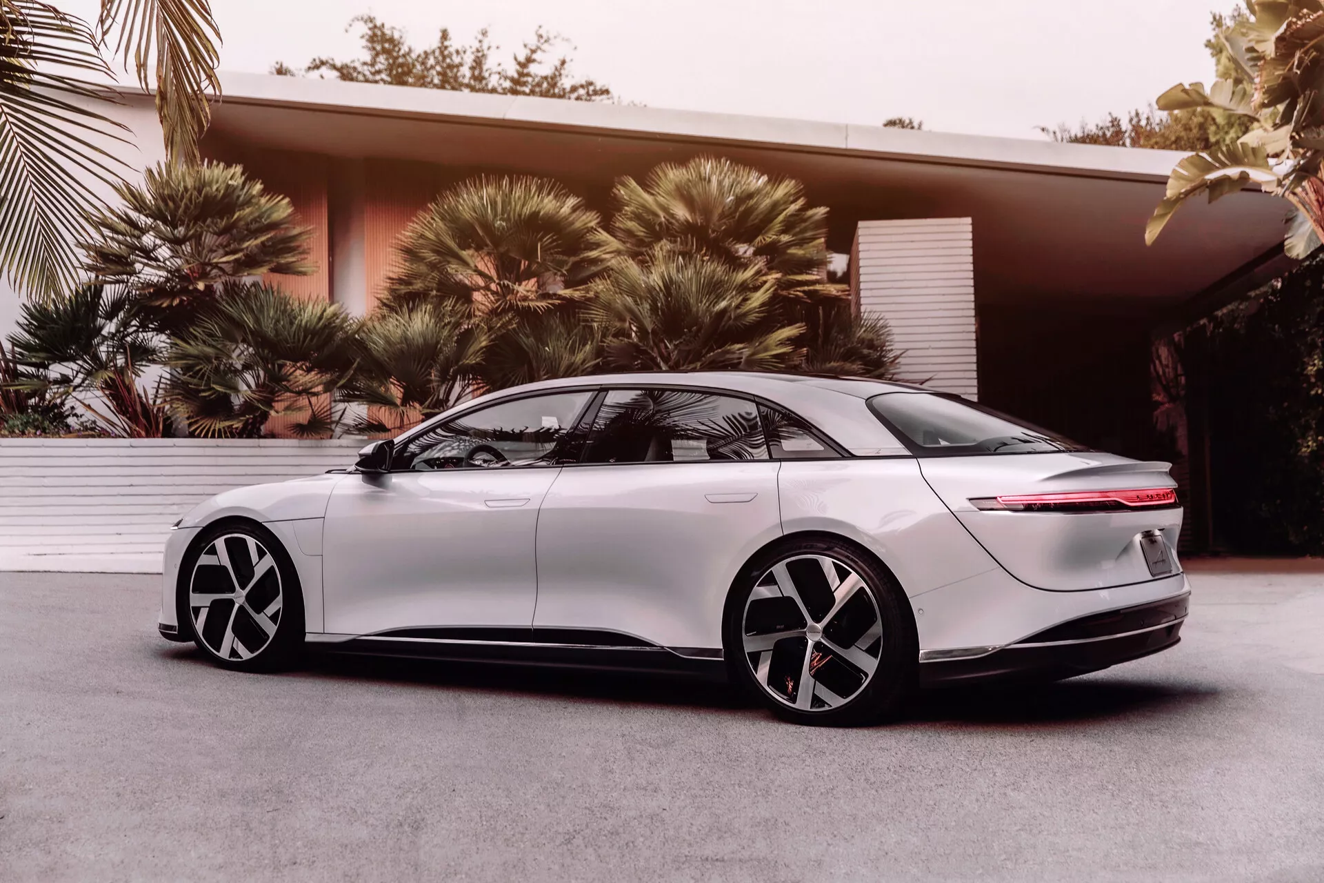 2022 Lucid Air elektryczny sedan, 1. generacja, widok z boku z niskiego kąta podkreślający aerodynamiczny design, eleganckie reflektory LED, gładki przedni błotnik, chowane uchwyty drzwiowe, dwukolorowe pięcioramienne felgi, przyciemniane szyby, tylna część fastback z poziomym paskiem świetlnym i zintegrowanym spoilerem, ukazujące nowoczesną technologię i design pojazdów elektrycznych.