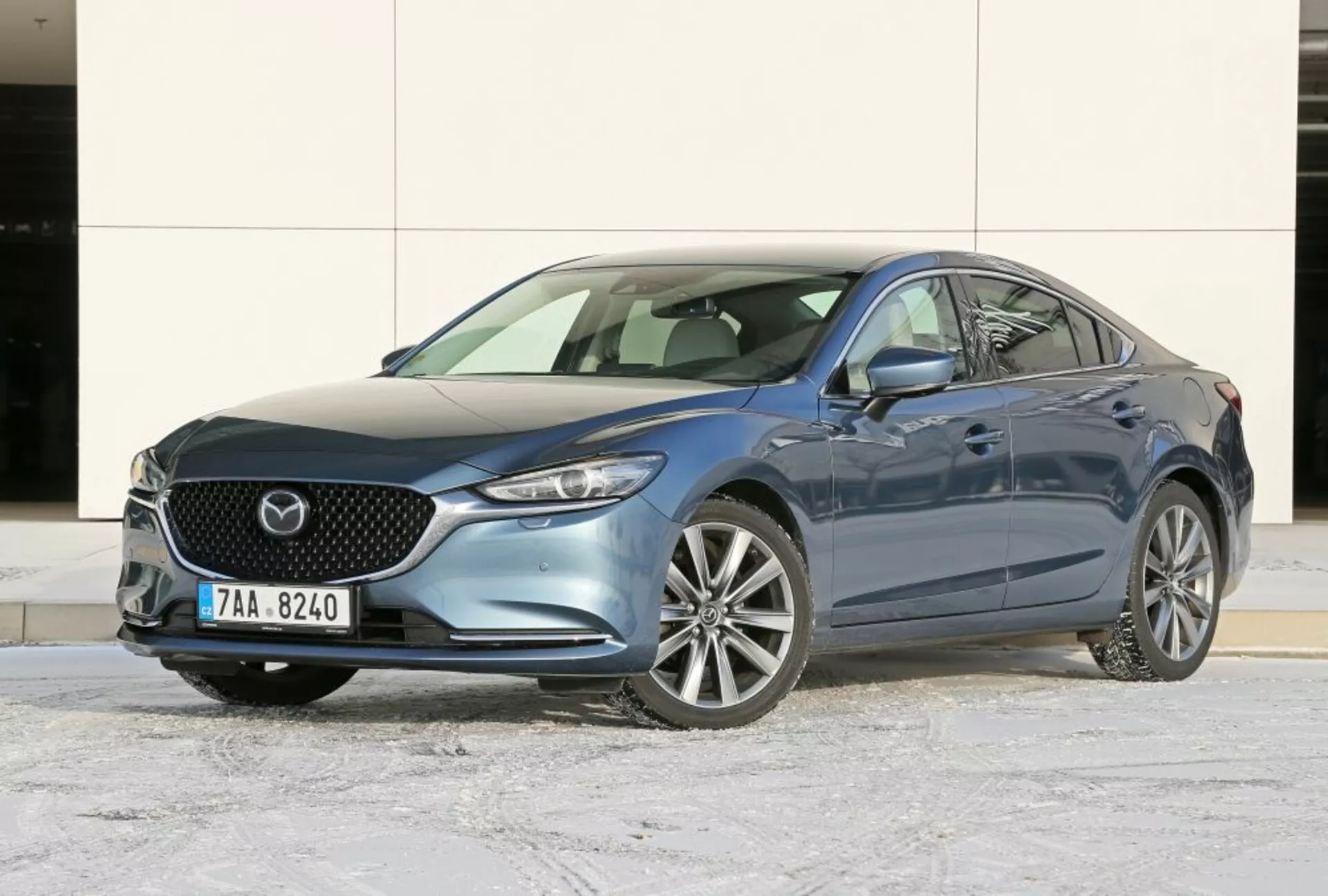 Sedan Mazda 6 z 2013 roku w kolorze niebieskim, prezentujący kąt przedni trzech czwartych dla wyraźnego widoku na grill, emblemat, eleganckie reflektory i aluminiowe koła na zimowym asfalcie
