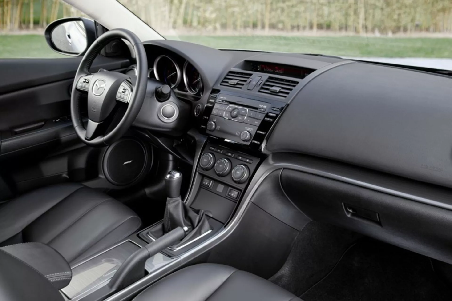 Wnętrze sedana Mazda 6 z 2008 roku prezentujące kokpit kierowcy i widok deski rozdzielczej pasażera z kontrolami na kierownicy, systemami infotainment i klimatyzacji oraz konsolą automatycznej skrzyni biegów, podkreślające nowoczesny design i technologiczne funkcje samochodu.