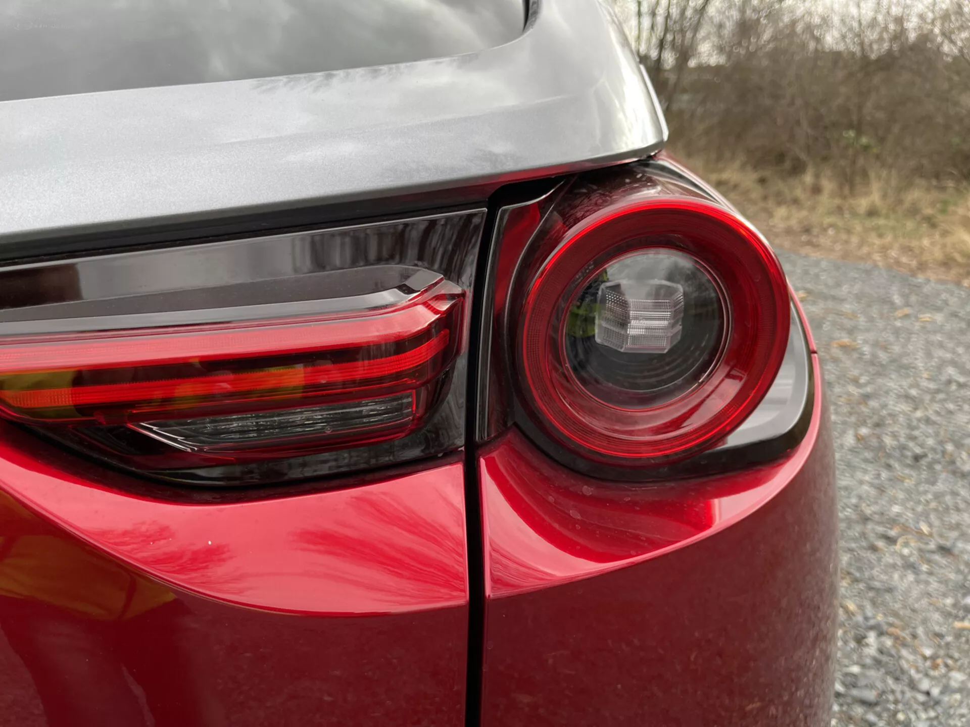 Zbliżenie na tylny narożnik Mazdy MX-30 2020 pokazujące szczegółowy design lampy tylnej, lśniący czerwony lakier i odbicie na karoserii, podkreślający nowoczesną technologię oświetlenia i design pojazdów.