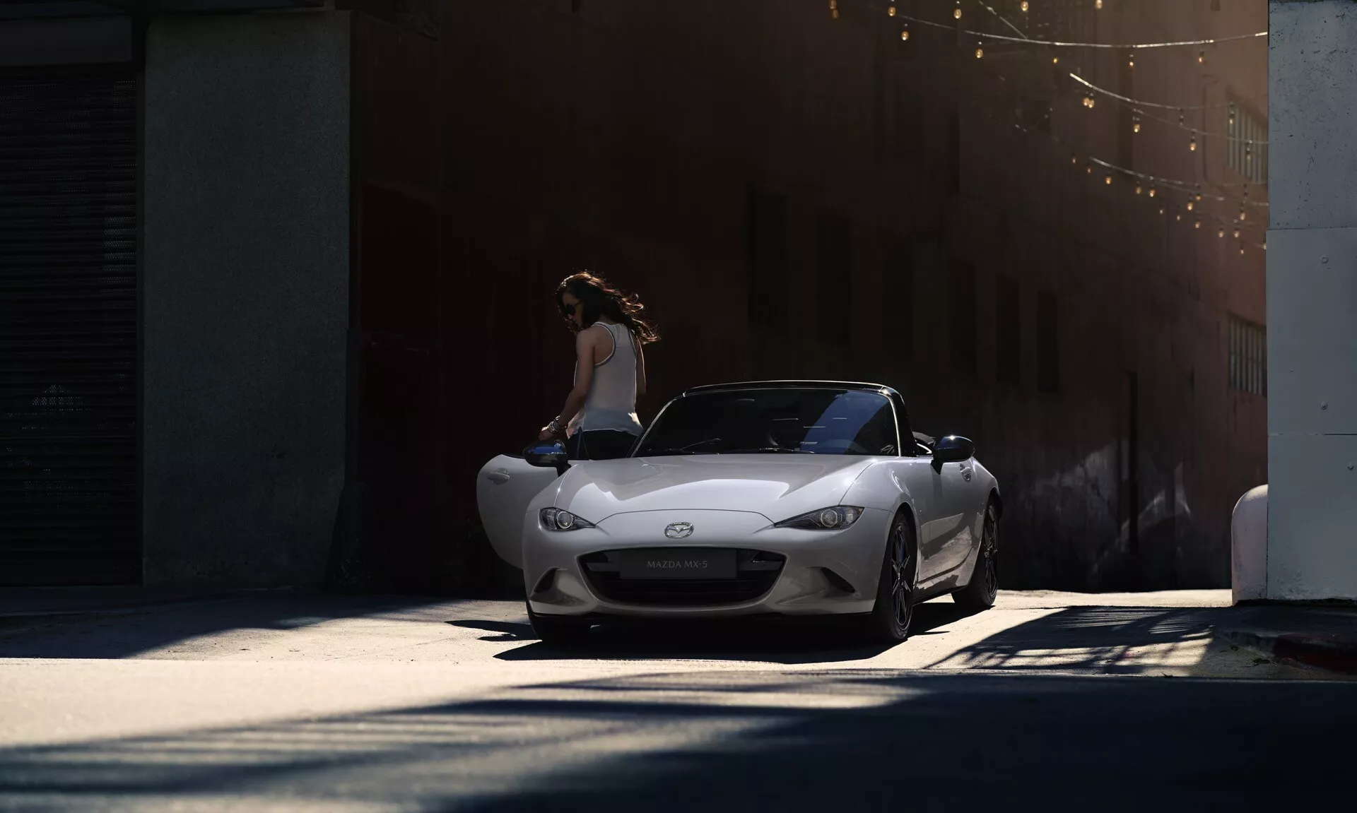 Srebrny kabriolet Mazda MX-5 Miata 2023 z przodu pod delikatnym oświetleniem, ukazujący charakterystyczną kratkę, reflektory LED i aerodynamiczny design, z osobą stojącą obok