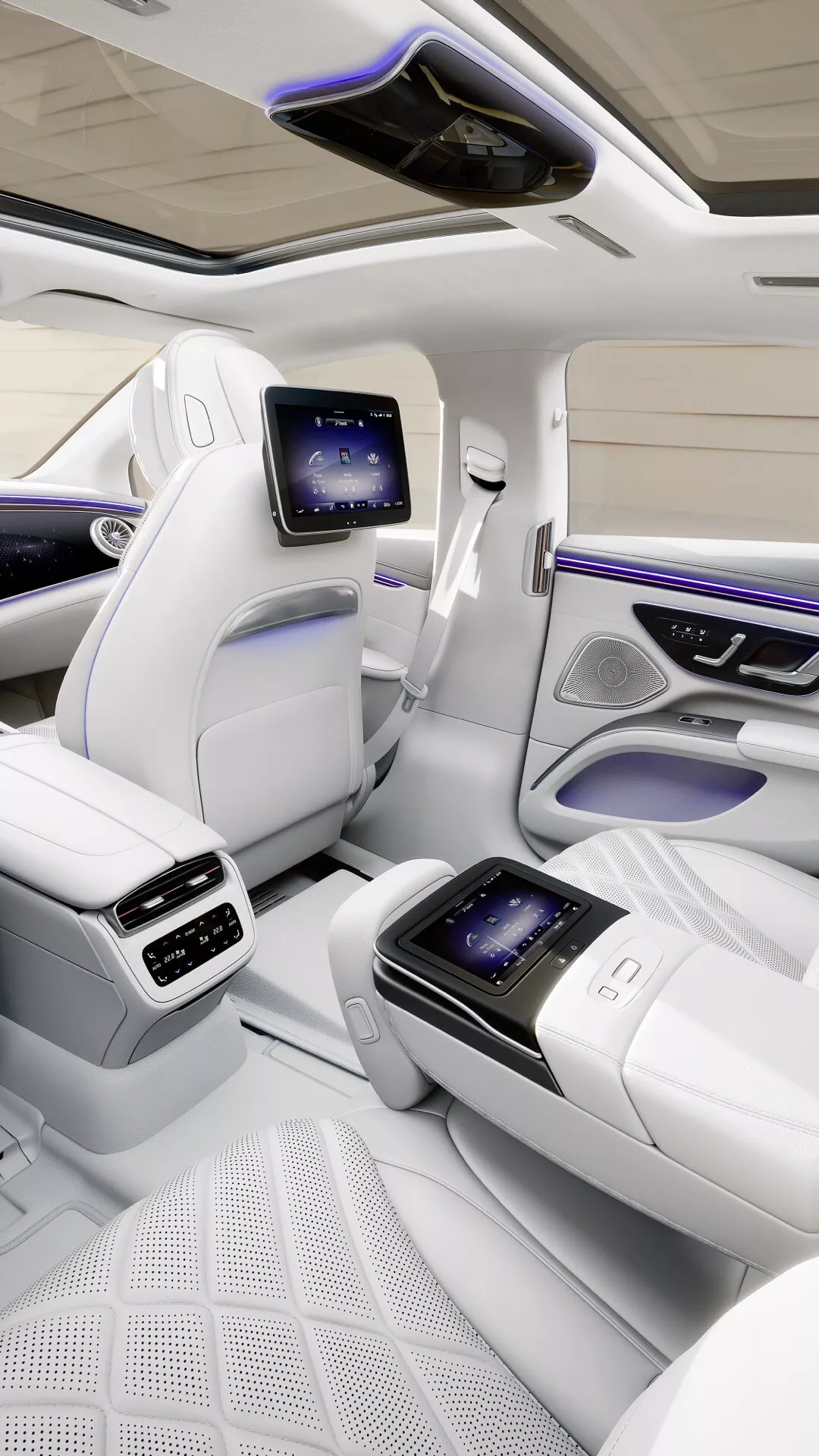 Widok wnętrza luksusowego samochodu Mercedes-Benz EQS 2024 przedstawiający tylną część komory pasażerskiej z przestronnymi siedzeniami, panoramicznym dachem, siedzeniami z białej skóry najwyższej jakości z pikowanym wzorem, ekranami rozrywki na tylne siedzenia i zaawansowanymi funkcjami technologicznymi
