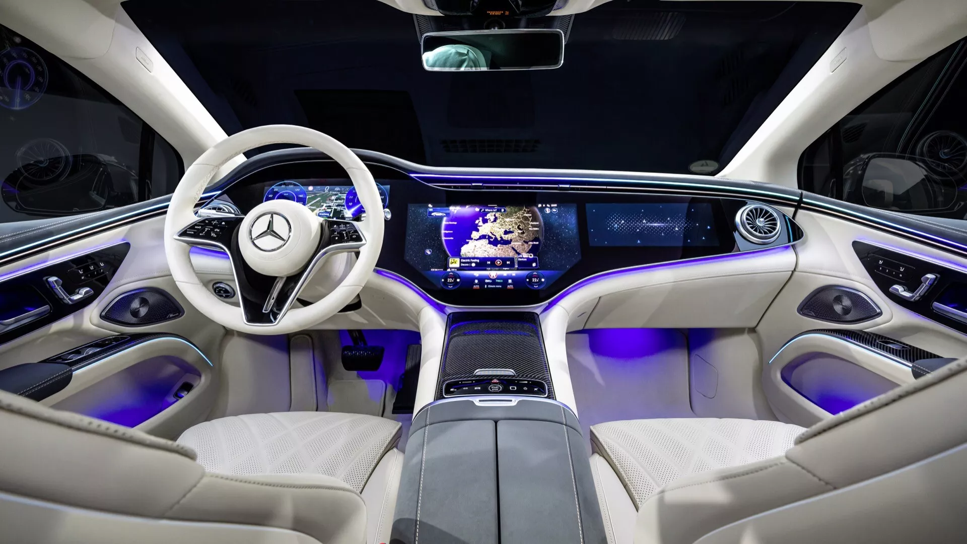 Wnętrze Mercedes-Benz EQS facelifting 2024 z perspektywy tylnych siedzeń podkreślające funkcje technologiczne i elementy luksusowe, w tym dwuramienną, luksusową kierownicę z przyciskami, elegancką deskę rozdzielczą z podwójnym ekranem, konsolę środkową z dotykowymi sterownikami, niebieskie oświetlenie ambientowe, kremowe skórzane siedzenia i panoramiczny dach