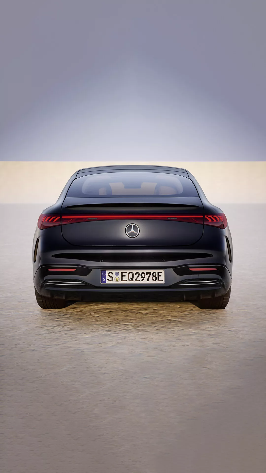 Tył Mercedes-Benz EQS lifting 2024 z paskiem świateł LED, czujnikami parkowania montowanymi na płasko i oznaczeniem pojazdu elektrycznego na odbijającej podłodze salonu