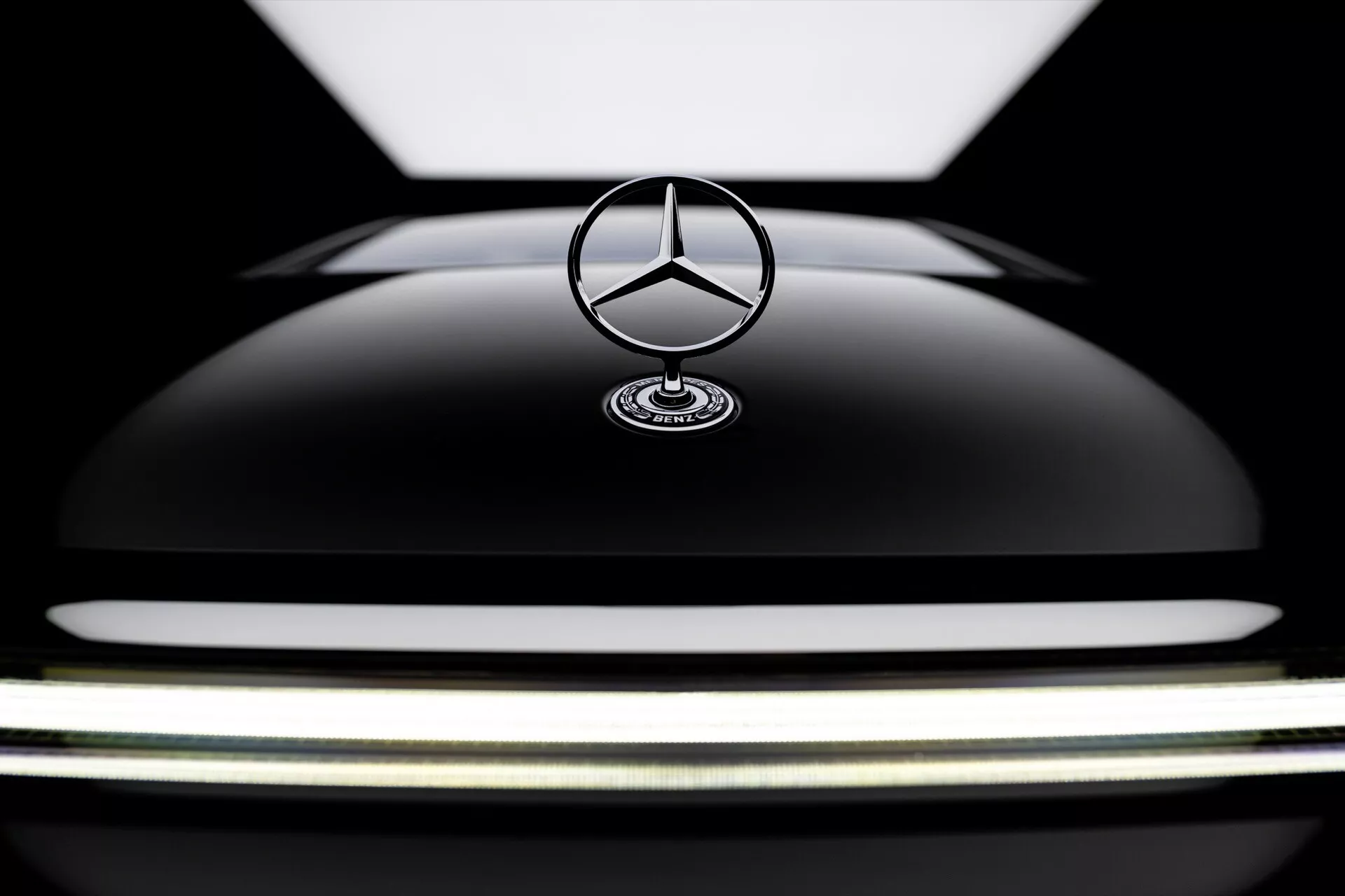 Zbliżenie na przednią część Mercedes-Benz EQS 2024 ze skupieniem na błyszczącym czarnym kapturze i ikonicznym emblematem gwiazdy, pokazujące luksusowy design i elegancką krzywiznę pojazdu.