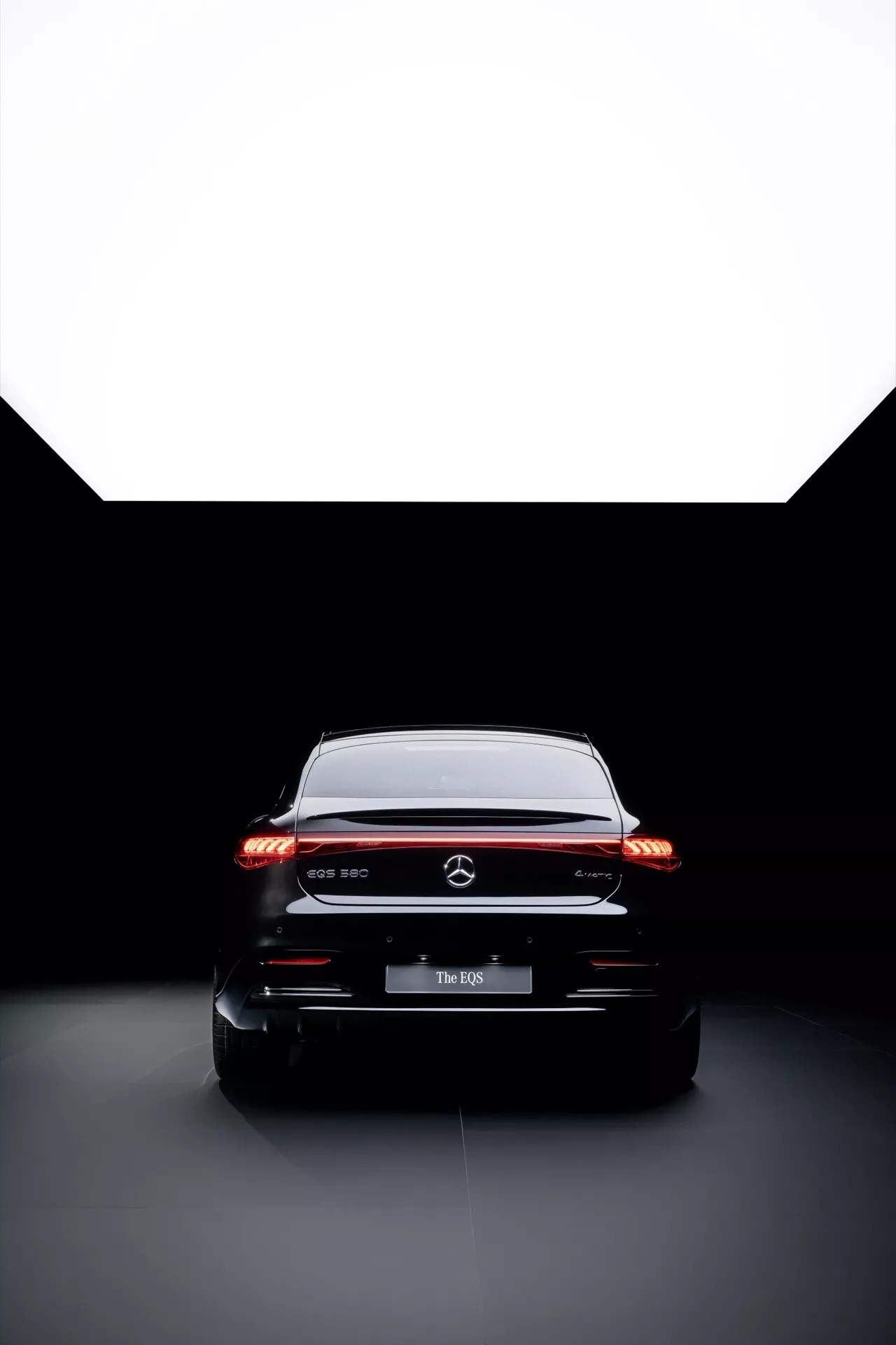 Zdjęcie studyjne tyłu Mercedes-Benz EQS 2024 przedstawiające diody LED w światłach tylnych, emblemat premium i oświetlenie o wysokim kontraście do szczegółowego badania współczesnego designu i technologii samochodów.