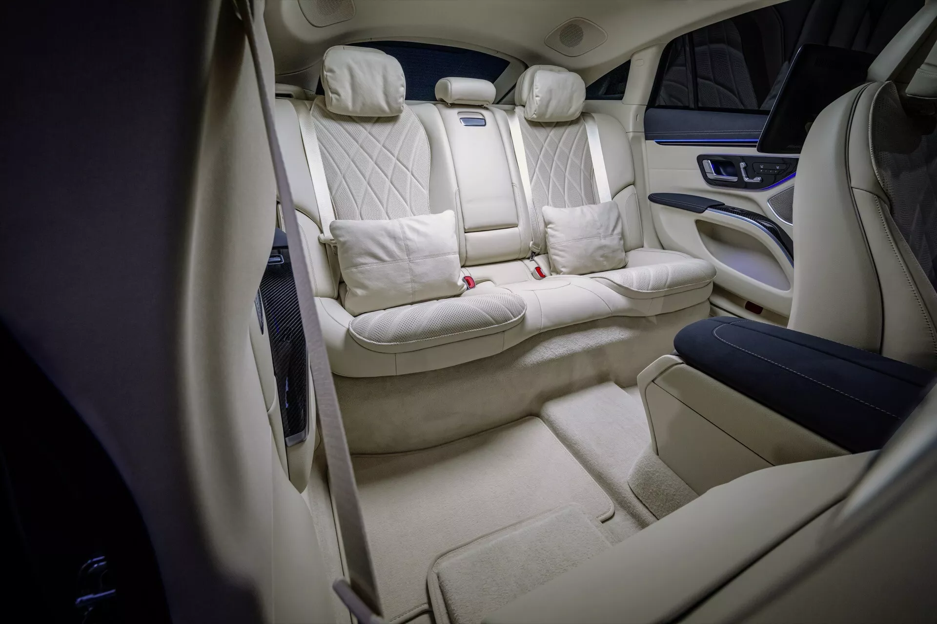 Widok wnętrza liftu Mercedes-Benz EQS 2024 ukazujący luksusową tylną kabinę z siedzeniami w pikowany wzór diamentowy, tapicerką w jasnym kremie, premium konsolą centralną, obszerną przestrzeń na nogi i oświetlenie ambientowe