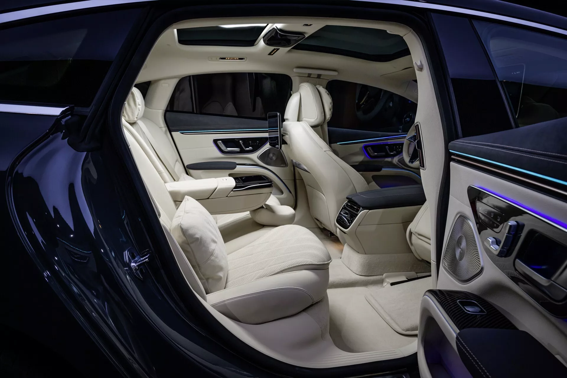 Pokaz wnętrza Mercedes-Benz EQS 297 lifting 2024 z sofistykowanymi jasnoskórzymi siedzeniami, elegancki design deski rozdzielczej z cyfrowym wyświetlaczem, wysokiej klasy panele drzwiowe z kontrolami, rozszerzona konsola centralna, system rozrywki dla pasażerów tylnych, podłoga z najwyższej jakości dywanikiem i ambientowe oświetlenie kabiny, widok z boku z otwartymi drzwiami pasażera przedniego.