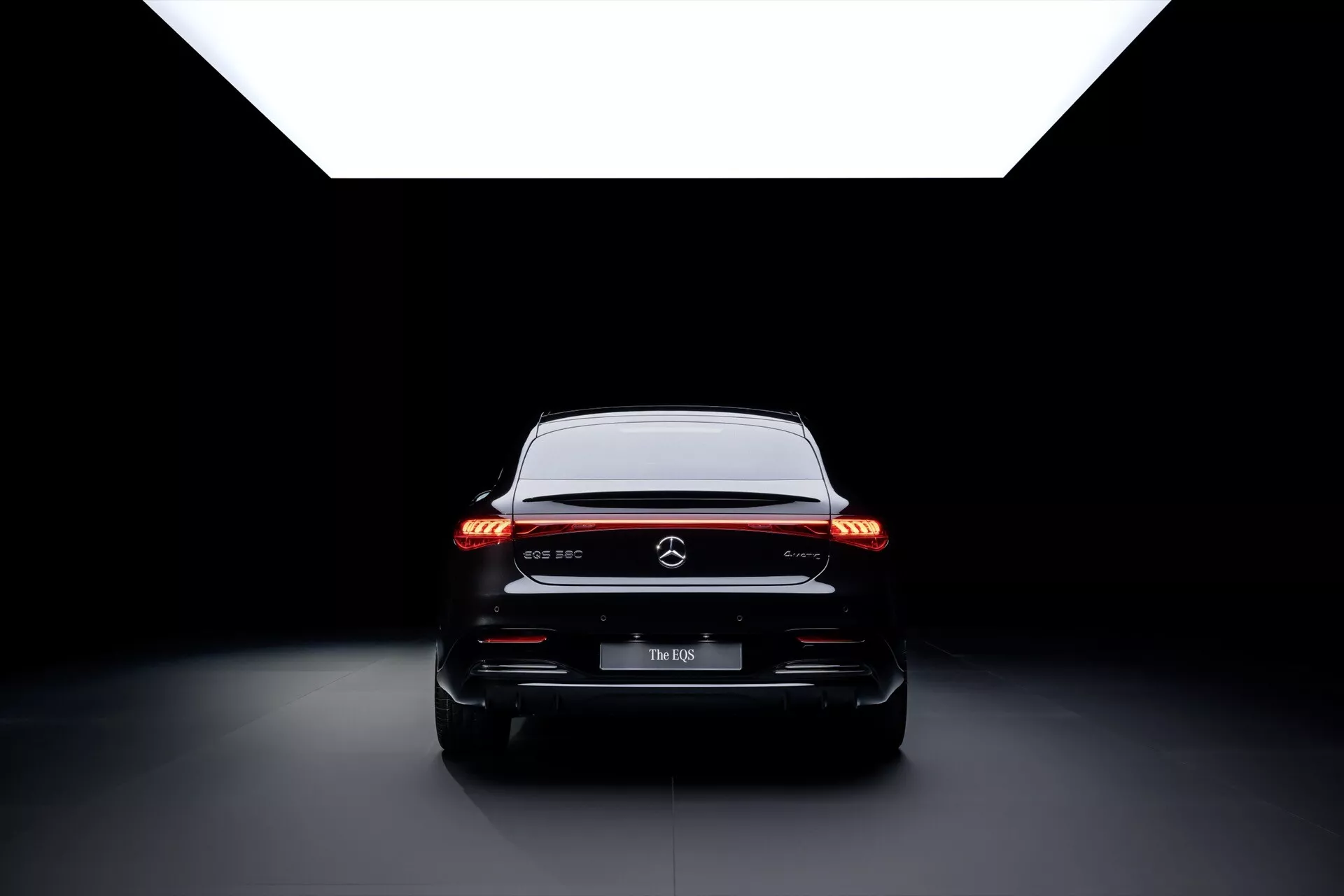 Tylny widok Mercedes-Benz EQS 297 facelifting 2024 ukazujący tylne światła LED z poziomym pasem świetlnym, błyszczącą czarną listwą i zaawansowaną aerodynamikę na ciemnym tle studia