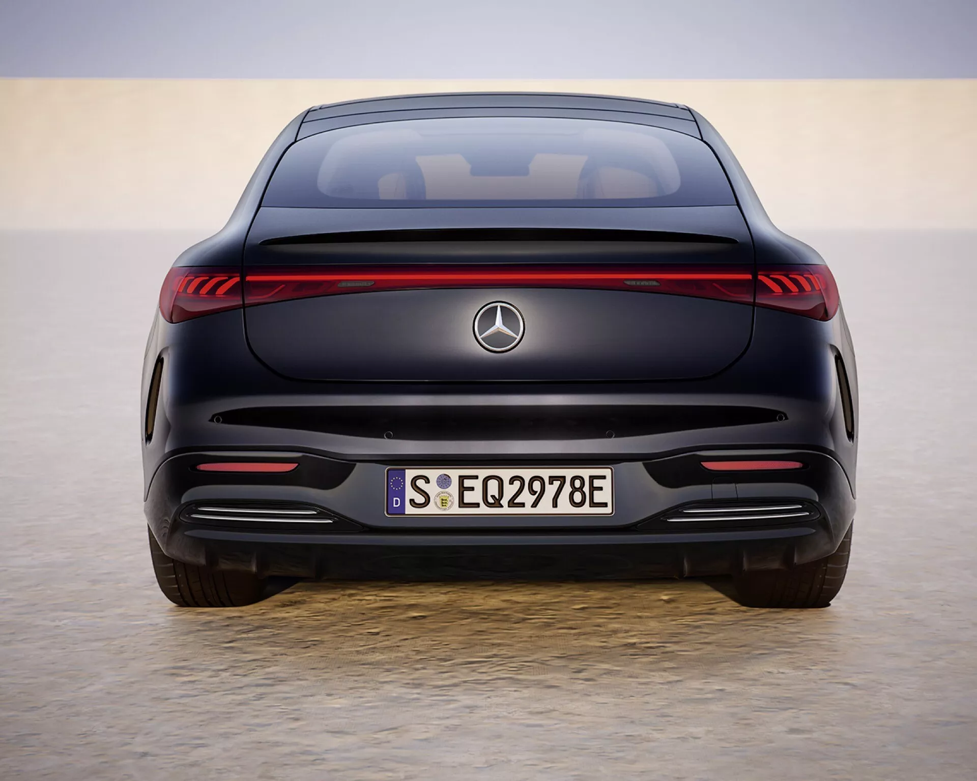 Tylny widok modelu Mercedes-Benz EQS 297 po liftingu z 2024 roku w scenerii przypominającej pustynię, prezentujący LEDowe światła tylne, oznaczenia EQ i sportowy design zderzaka w świetle dziennym