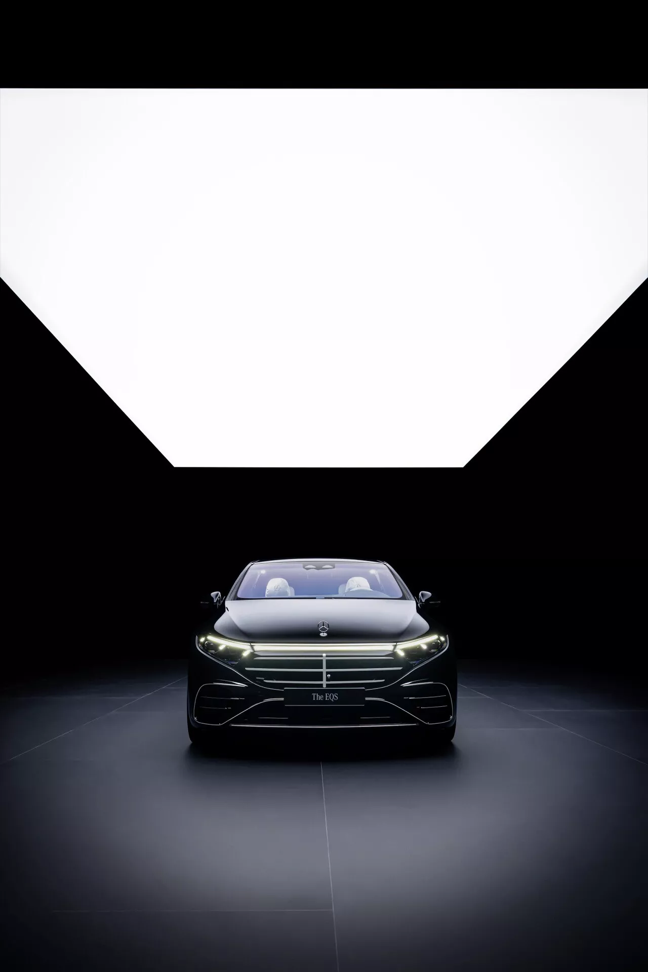 Facelifting Mercedes-Benz EQS 2024 z widokiem z przodu, oświetlonymi reflektorami LED i wyrazistym grillem, ujętym z niskiego kąta, aby podkreślić elegancki design i aerodynamiczne kontury na dramatycznie oświetlonym tle.