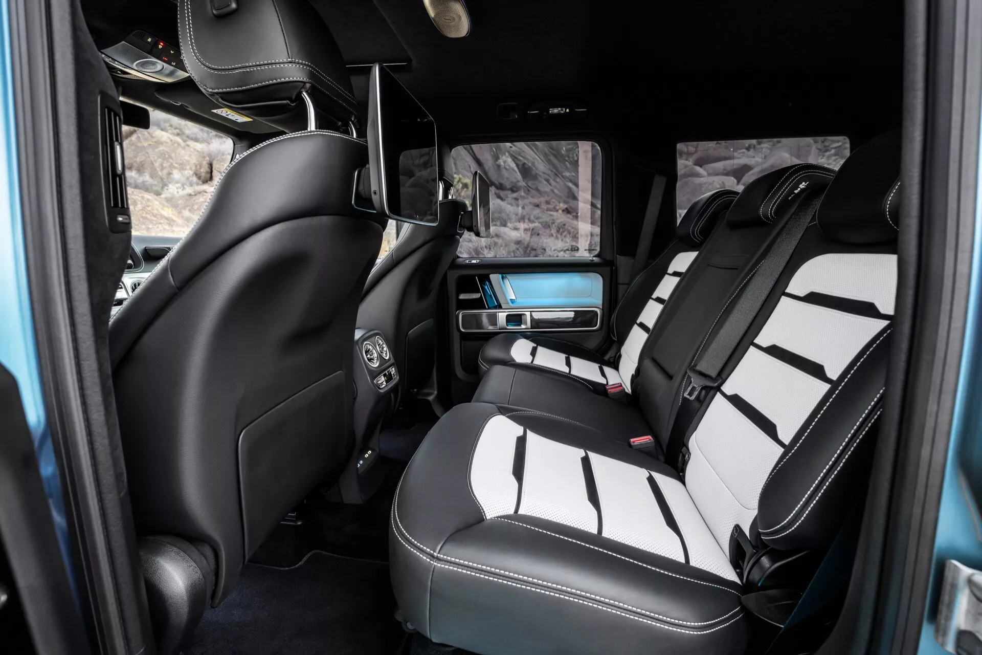 Wnętrze Mercedes-Benz G-Klasse 2024 skupiające się na luksusowej tylnej części pasażerskiej, prezentujące dwukolorowe skórzane siedzenia, konsolę środkową, kontrolę klimatu, system rozrywki i szczegóły wykończenia wysokiej klasy