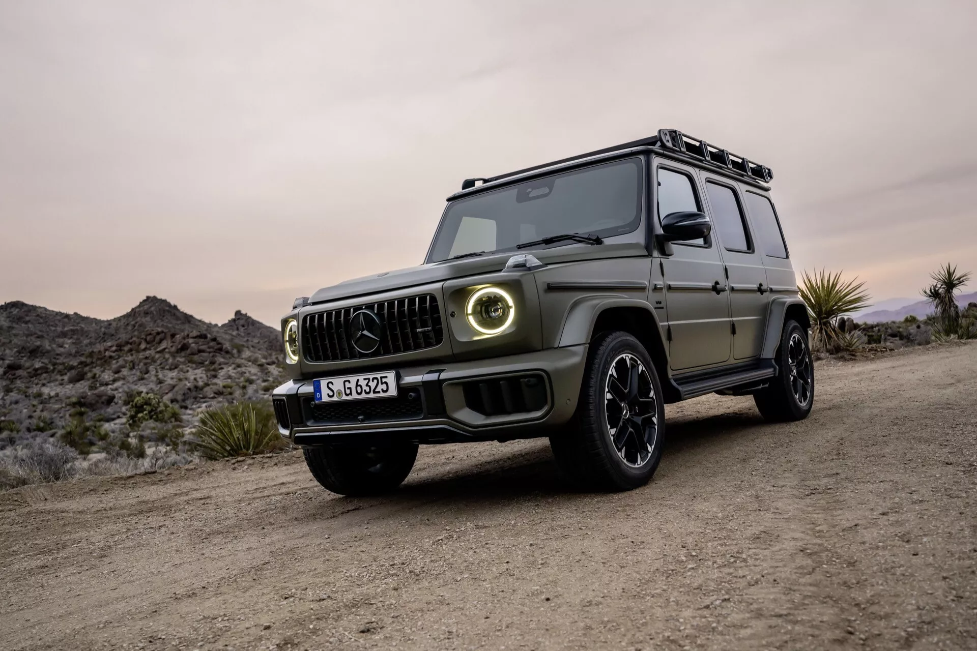 Luksusowy SUV Mercedes-Benz Klasa G 2024 w widoku z przodu trzy czwarte, prezentujący nowoczesny design, reflektory LED i zdolności terenowe na nieutwardzonej powierzchni