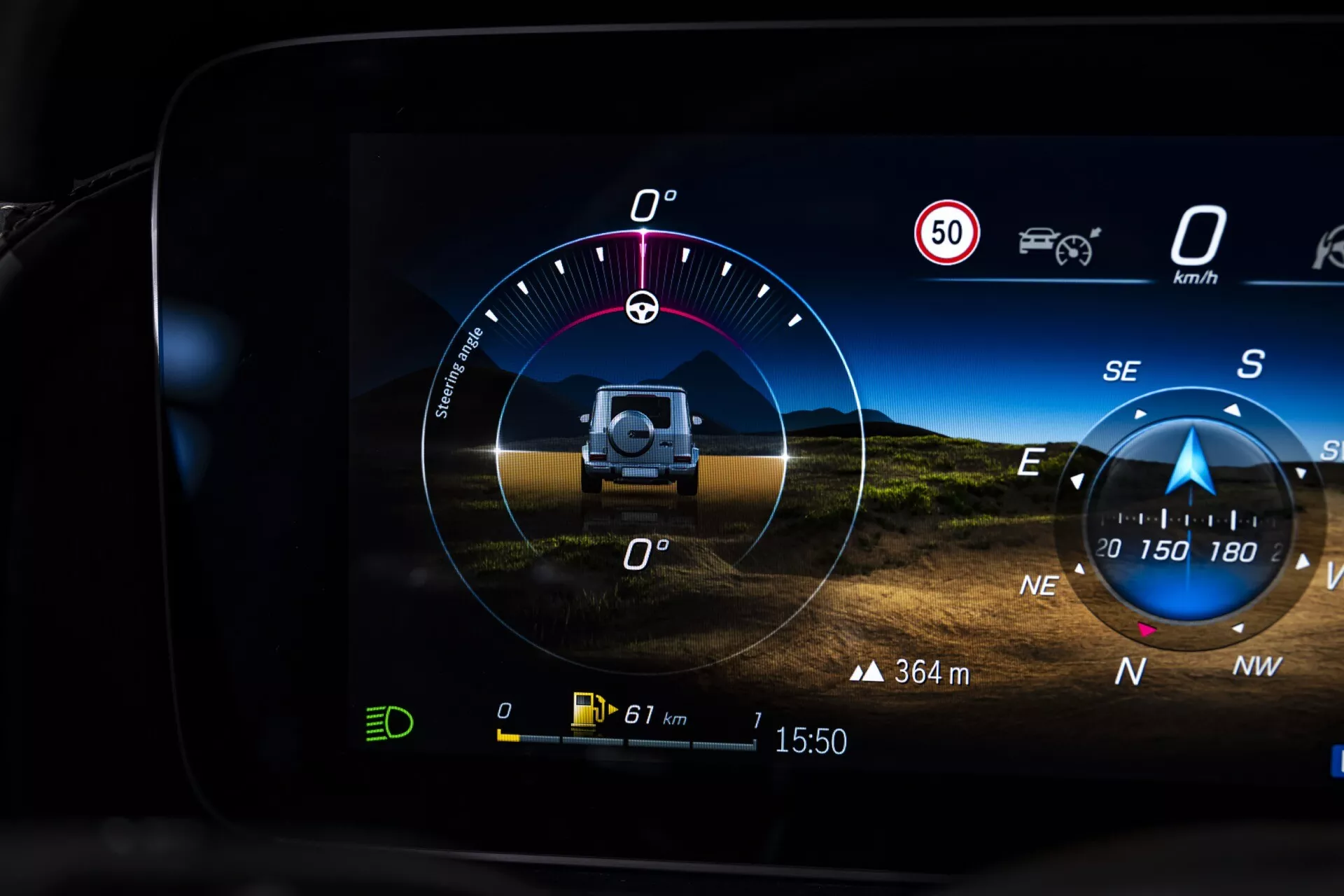 Cyfrowy kokpit Mercedes-Benz klasy G (G-Klasse) 2024 wyświetlający inklinometr terenowy, ograniczenie prędkości, kierunek wiatru, dane o nachyleniu i przechyle, kompas, zasięg pojazdu, temperaturę zewnętrzną i czas, co wskazuje na zaawansowane systemy nawigacji i asysty kierowcy