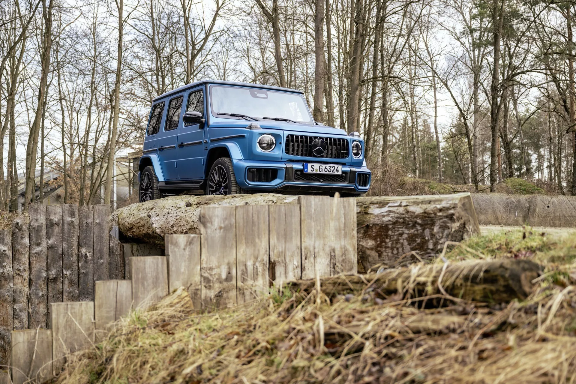 SUV Mercedes-Benz G-Klasse (Klasa G) 465 z 2024 r. prezentujący swoje zdolności terenowe na wielopoziomowej drewnianej rampie w trudnym terenie, podkreślający wysokie prześwit, solidną przednią kratę, reflektory LED i grube opony z głębokim bieżnikiem odpowiednie do trudnych warunków