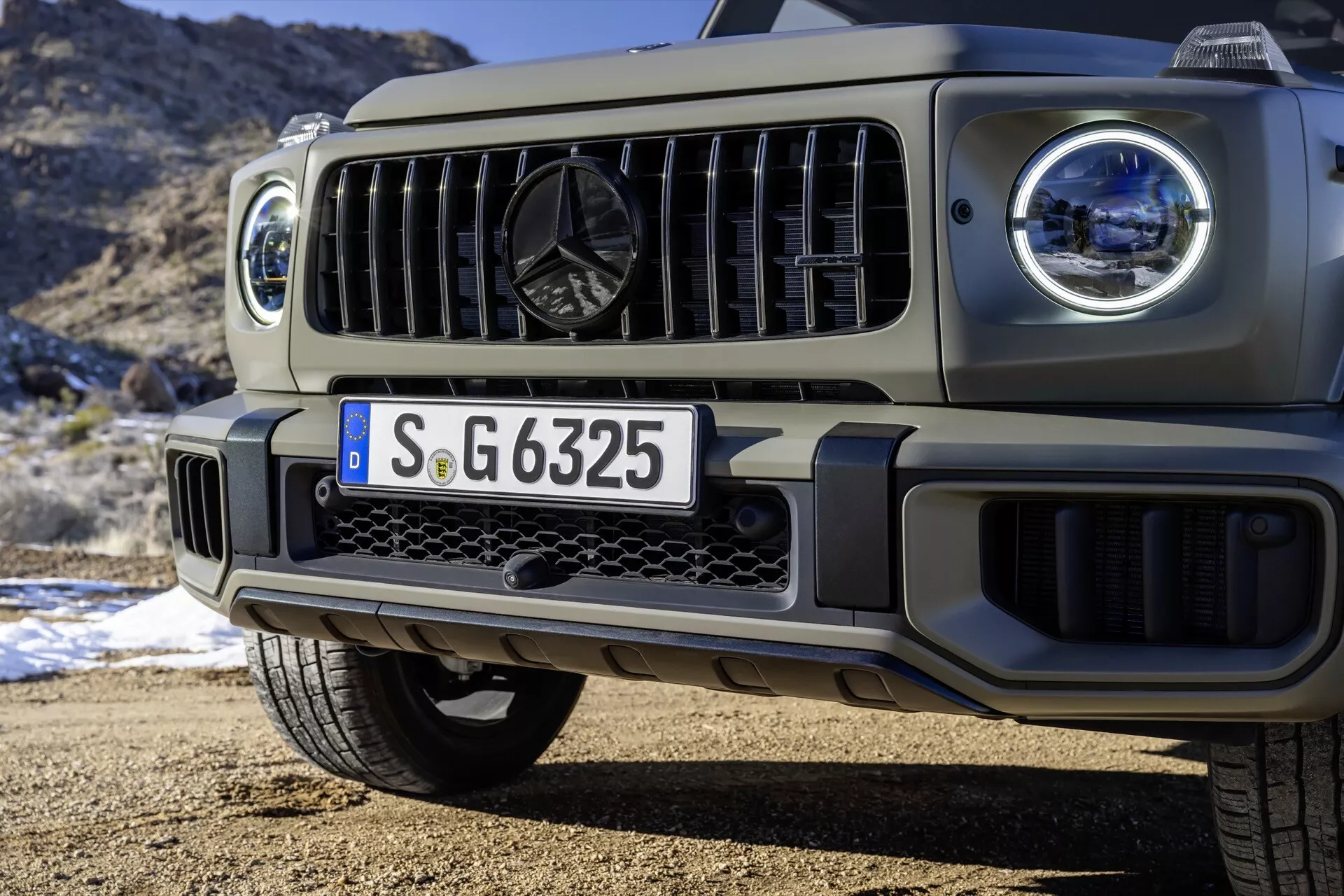 Zbliżenie na przednią część SUV-a Mercedes-Benz G-Class 2024, podkreślające reflektory LED, grill oraz design zderzaka przedniego na tle natury