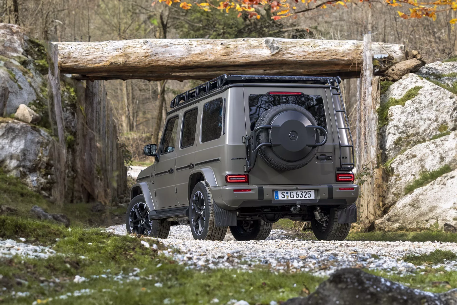 Tylny, kątowy widok SUV Mercedes-Benz G-Klasse 465 rocznik 2024, podkreślający wysokość i prześwit nad skalistym terenem, wyposażony w koło zapasowe, odbiornik haka holowniczego i pokazujący jego zdolności terenowe