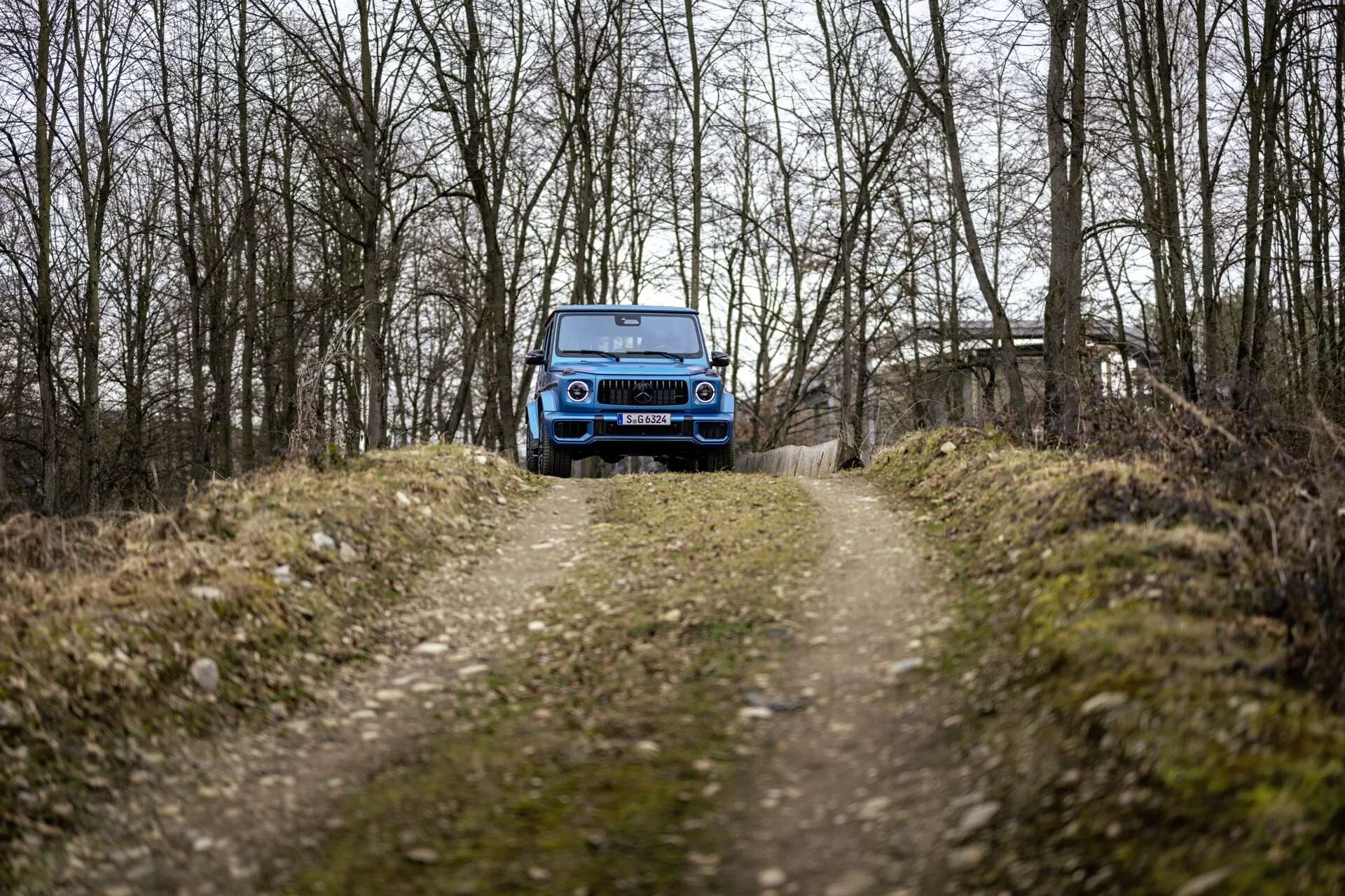 Niebieskie SUV Mercedes-Benz G-Klasse 465 rocznik 2024 na leśnej drodze ukazujące przedni grill, reflektory LED i zdolności terenowe