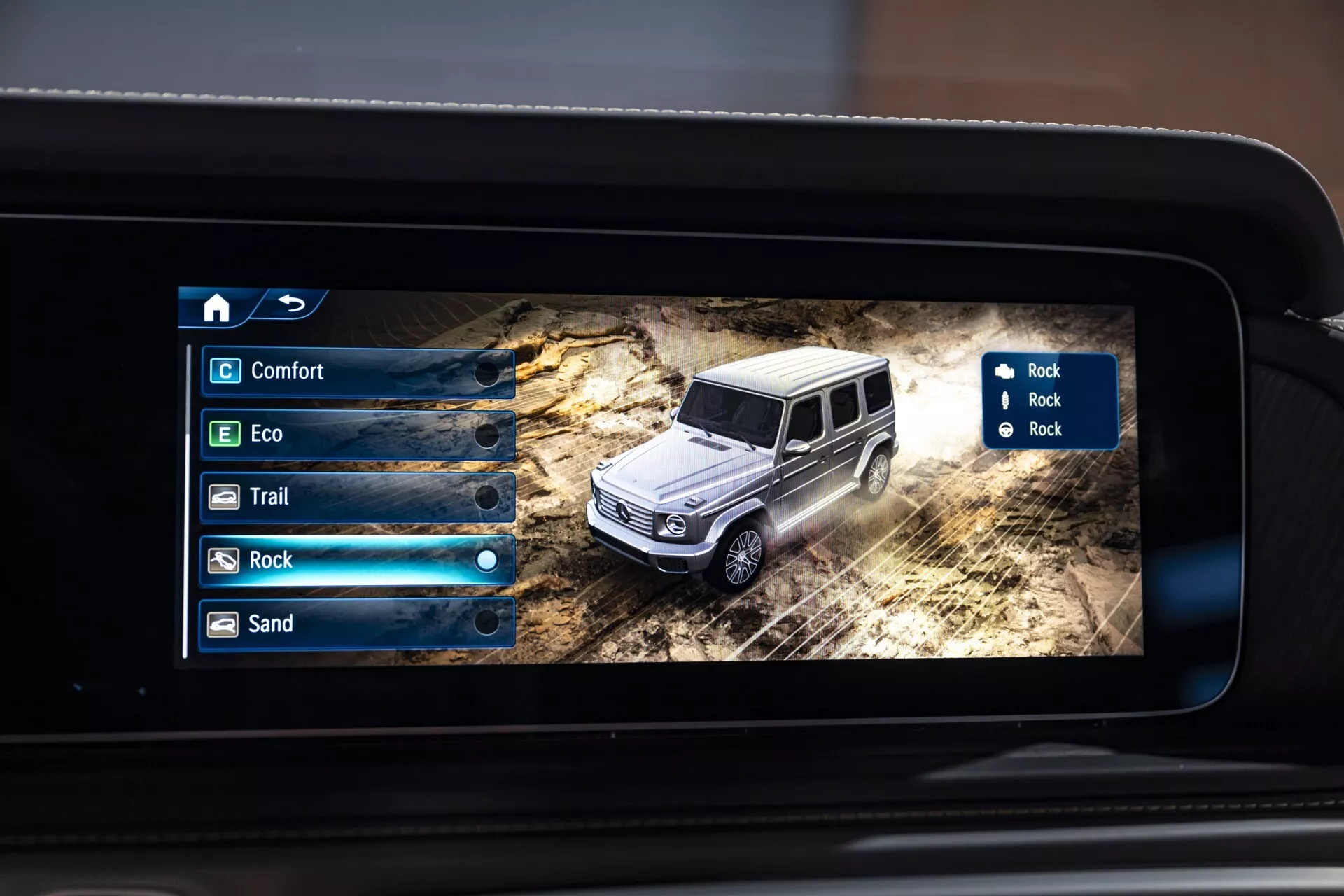 Zbliżenie cyfrowego wyświetlacza wewnątrz Mercedesa-Benz Klasy G 2024 prezentującego model 3D SUV-a w terenowym otoczeniu z opcjami trybów terenowych na ekranie