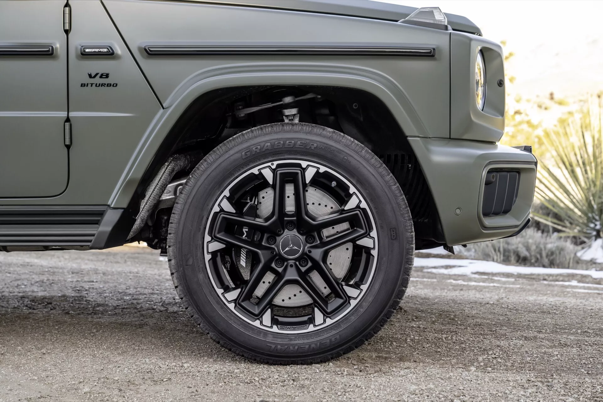 Zbliżenie na przednie koło pasażera i część profilu boczne Mercedes-Benz G-Klasse 2024, prezentujące wysokowydajny system hamulcowy i wieloramienne aluminiowe koło, w matowooliwkowej zieleń