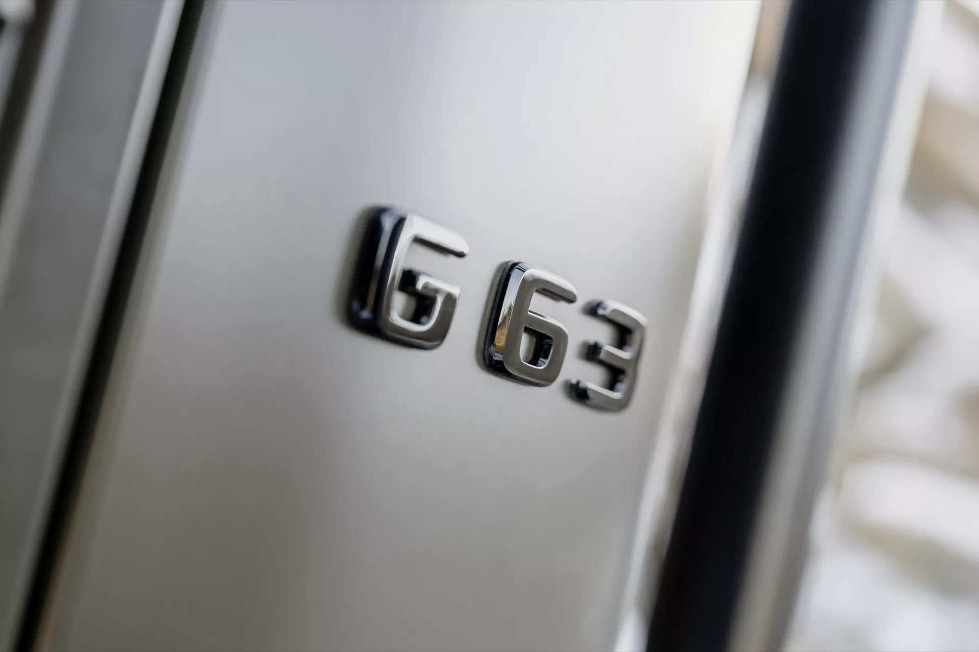 Zbliżenie na emblemat modelu Mercedes-Benz G63 z chromowanym wykończeniem na błotniku samochodu, podkreślające cechy luksusu i wydajności