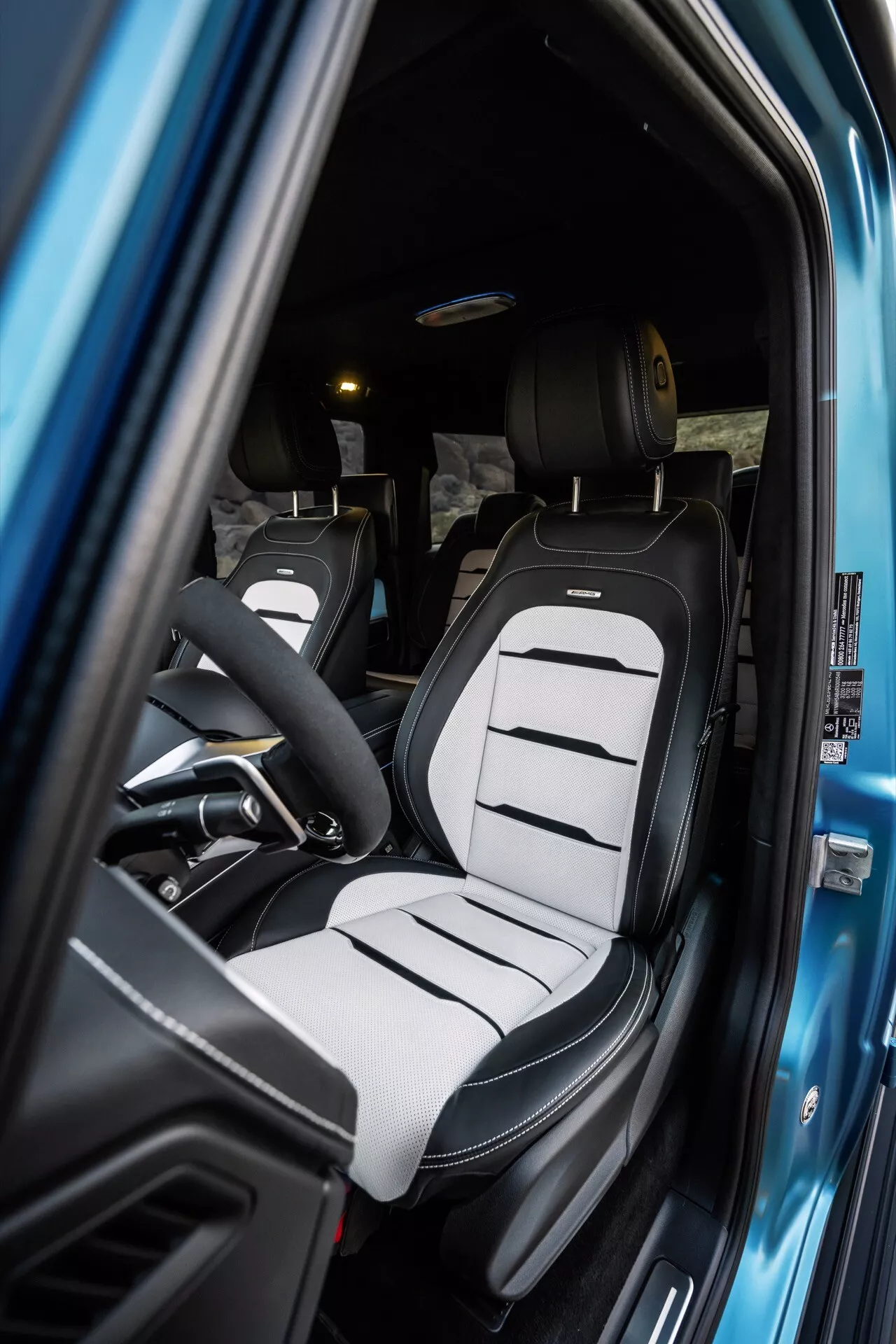 Widok wnętrza Mercedes-Benz G-Klasse (465) 2024 skupiający się na fotelu kierowcy z dwukolorową tapicerką i nowoczesnym designem fotela kubełkowego przez otwarte drzwi