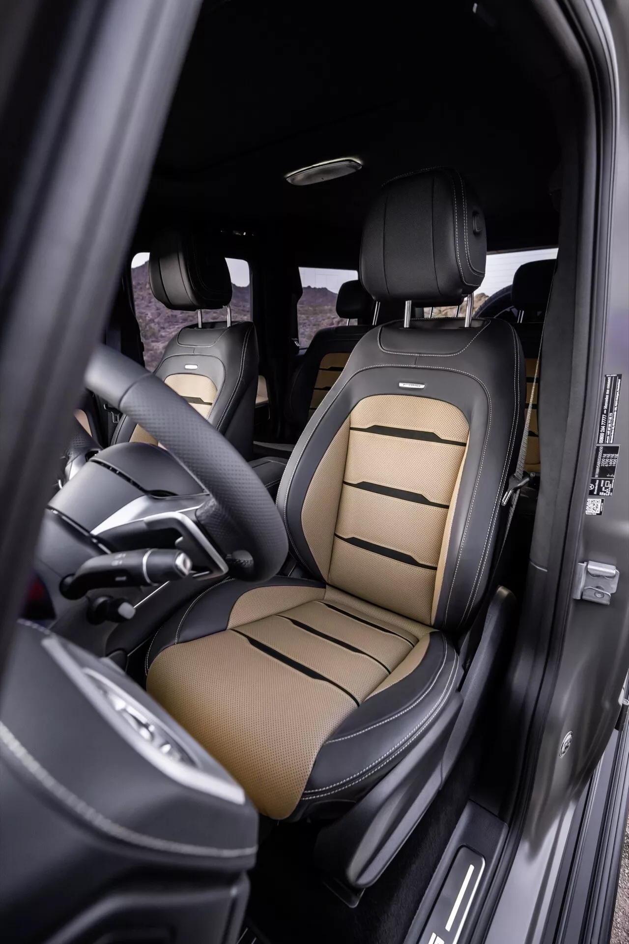 Widok wnętrza Mercedes-Benz G-Klasse 2024 z akcentem na fotel kierowcy z luksusową, dwukolorową tapicerką skórzaną, zaawansowanymi funkcjami regulacji fotela i elementami designu premium